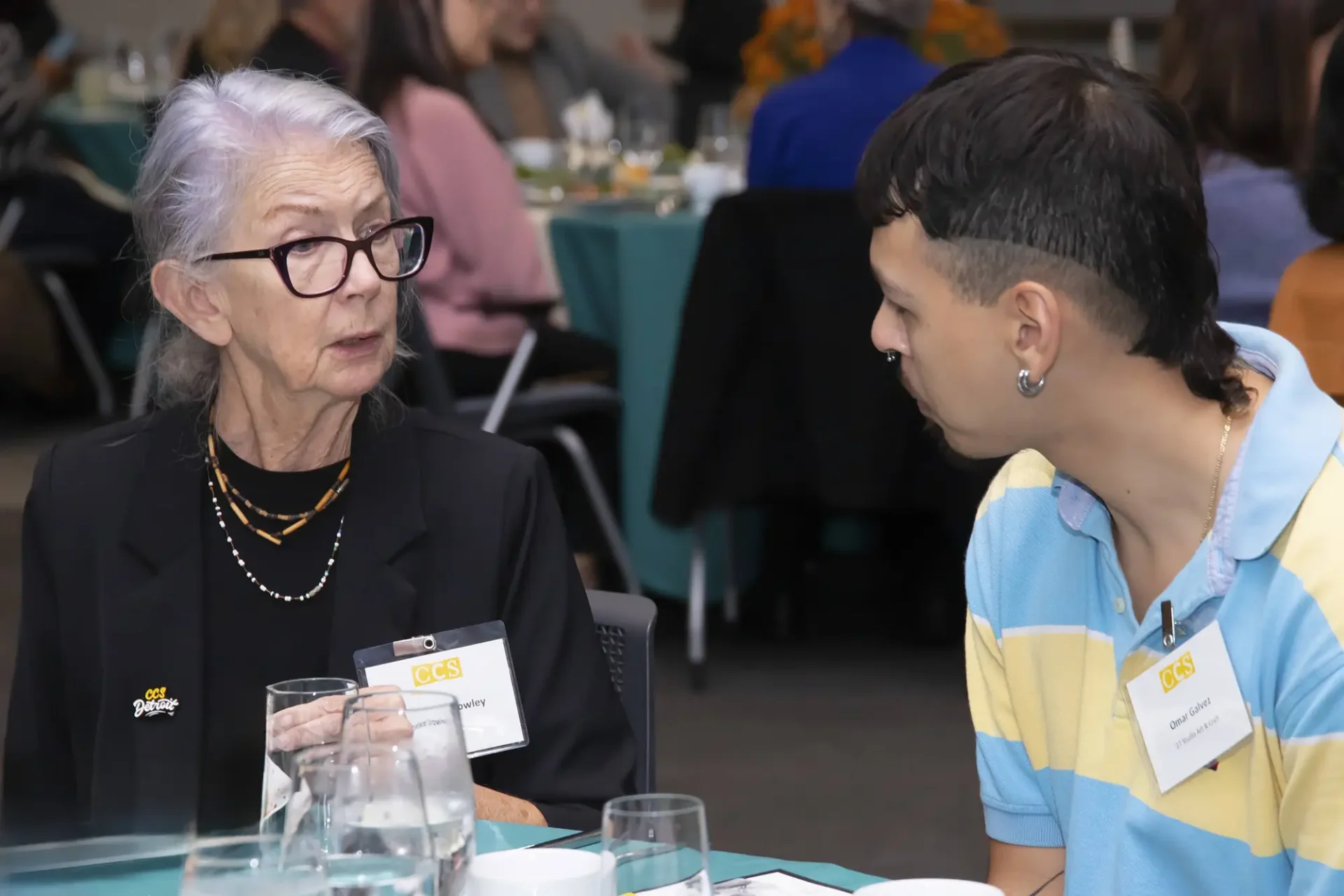 Two people engage in conversation at a dining table during an event.