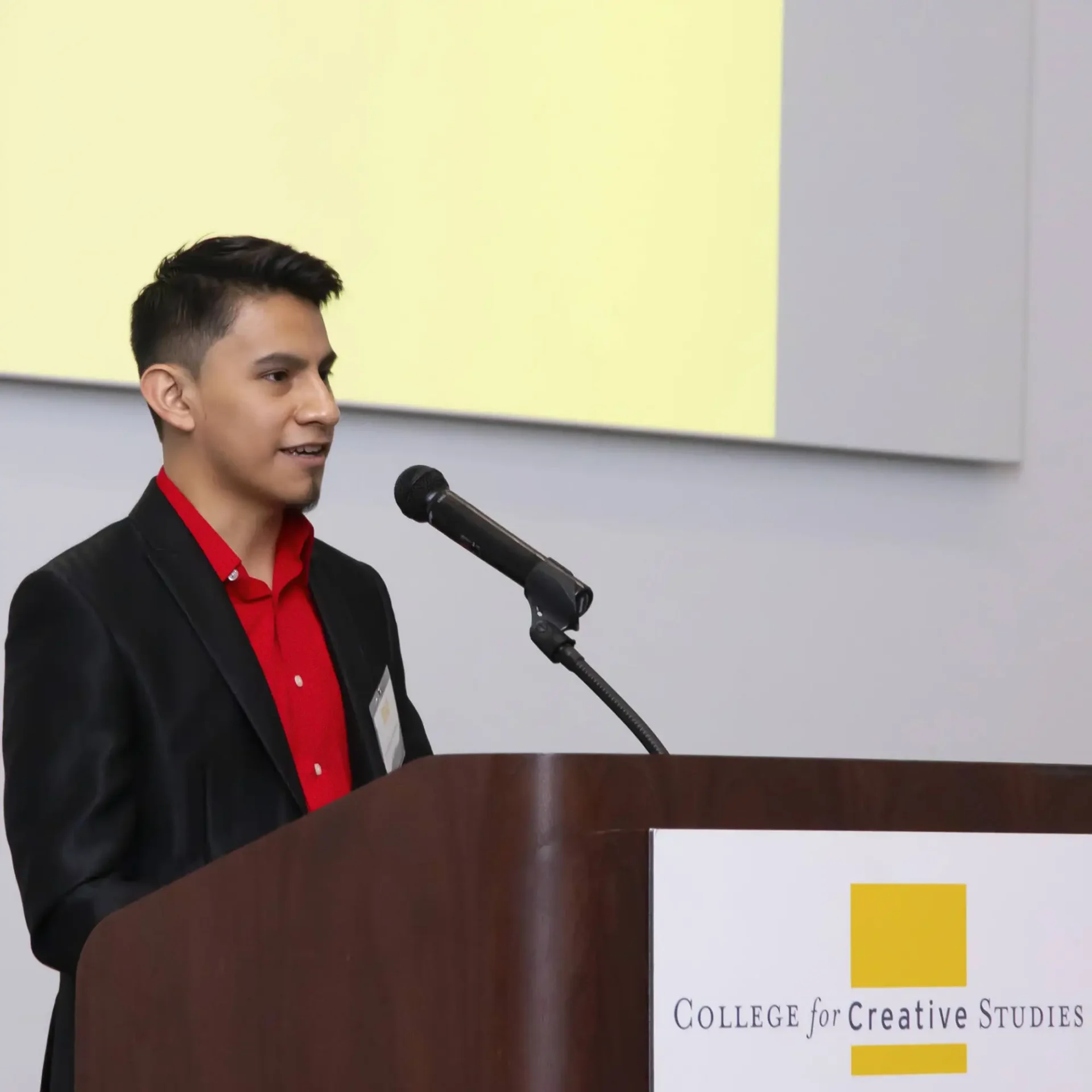 A young man speaks into a microphone at a wooden podium during an event.