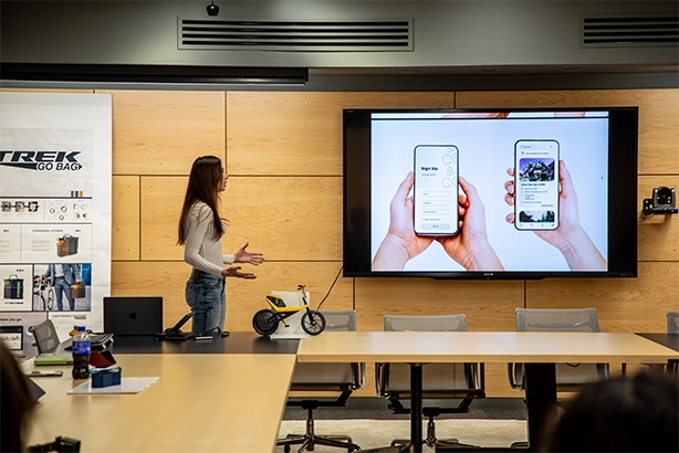 A student is presenting a concept in a board room to Trek designers for a sponsored studio project.