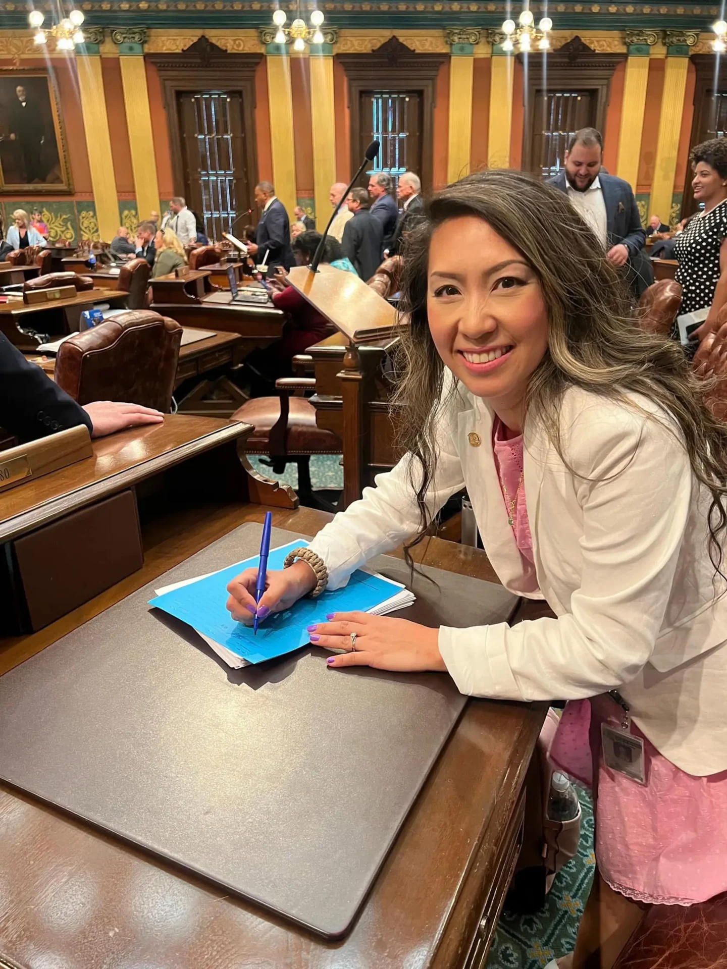 State Representative Mai Xiong writes on a blue sheet of paper while seated in the Michigan House chamber.