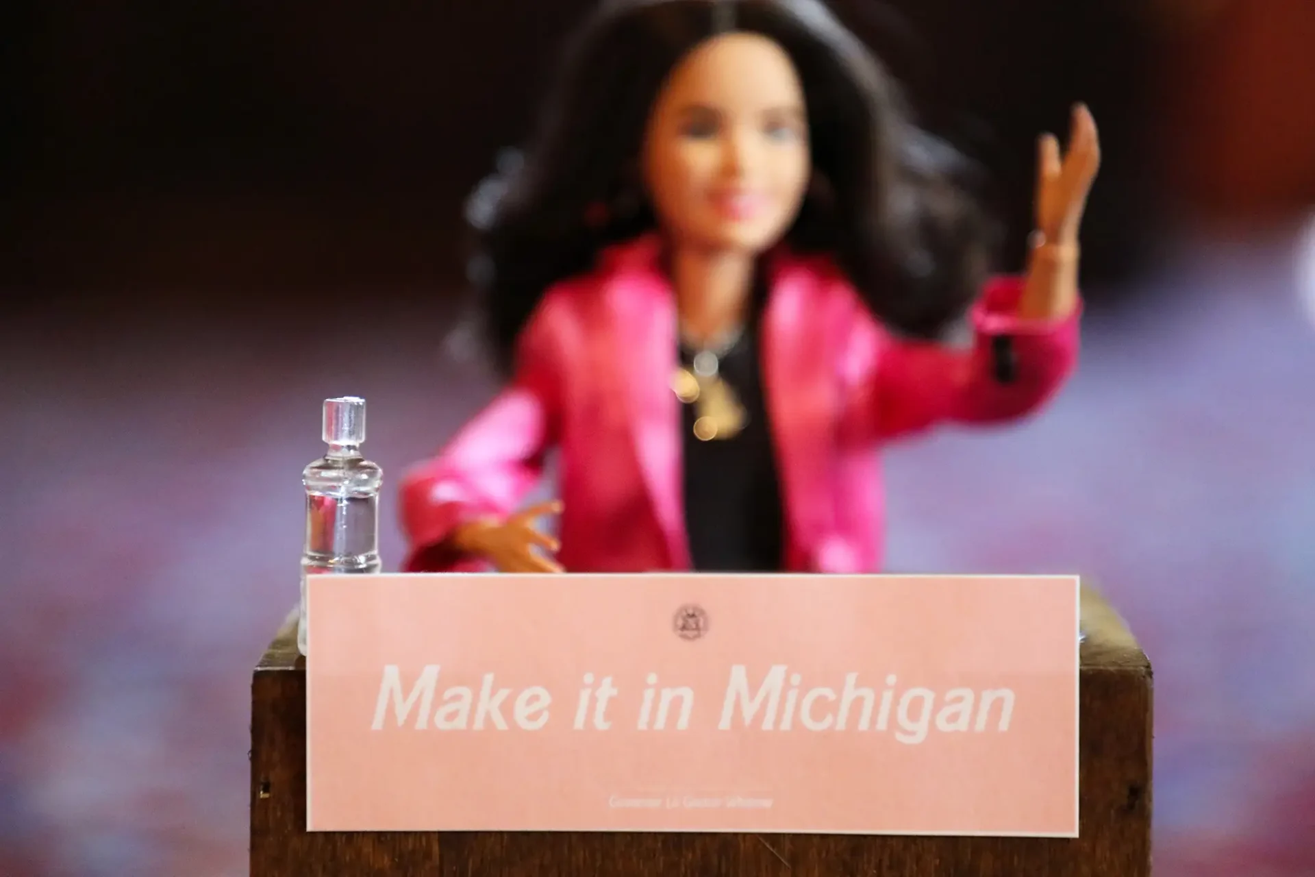 Lil Gretch Barbie doll stands behind a podium displaying a "Make it in Michigan" sign.
