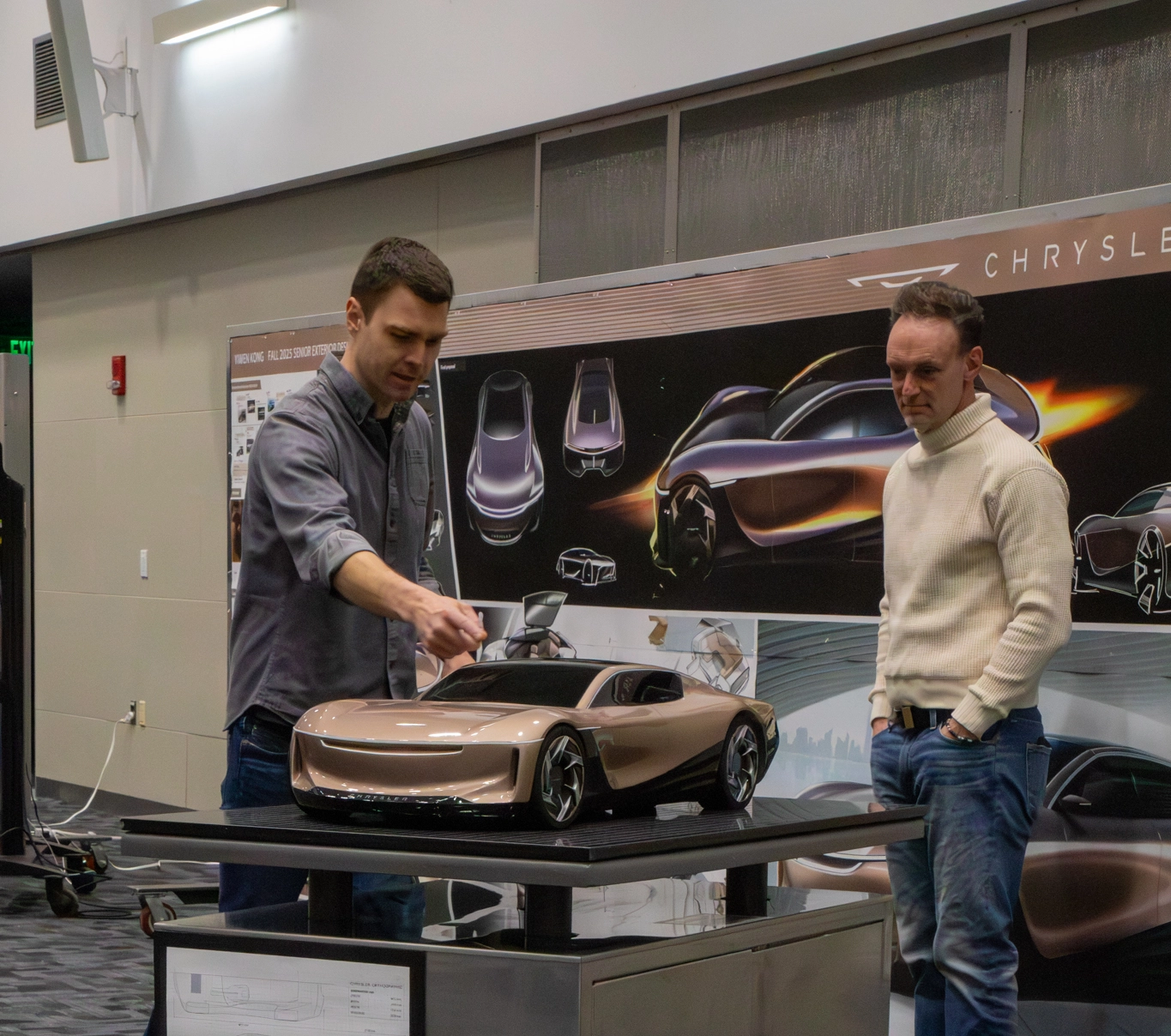 A student presents his gold car model to a designer during the Stellantis Sponsored Project final presentation