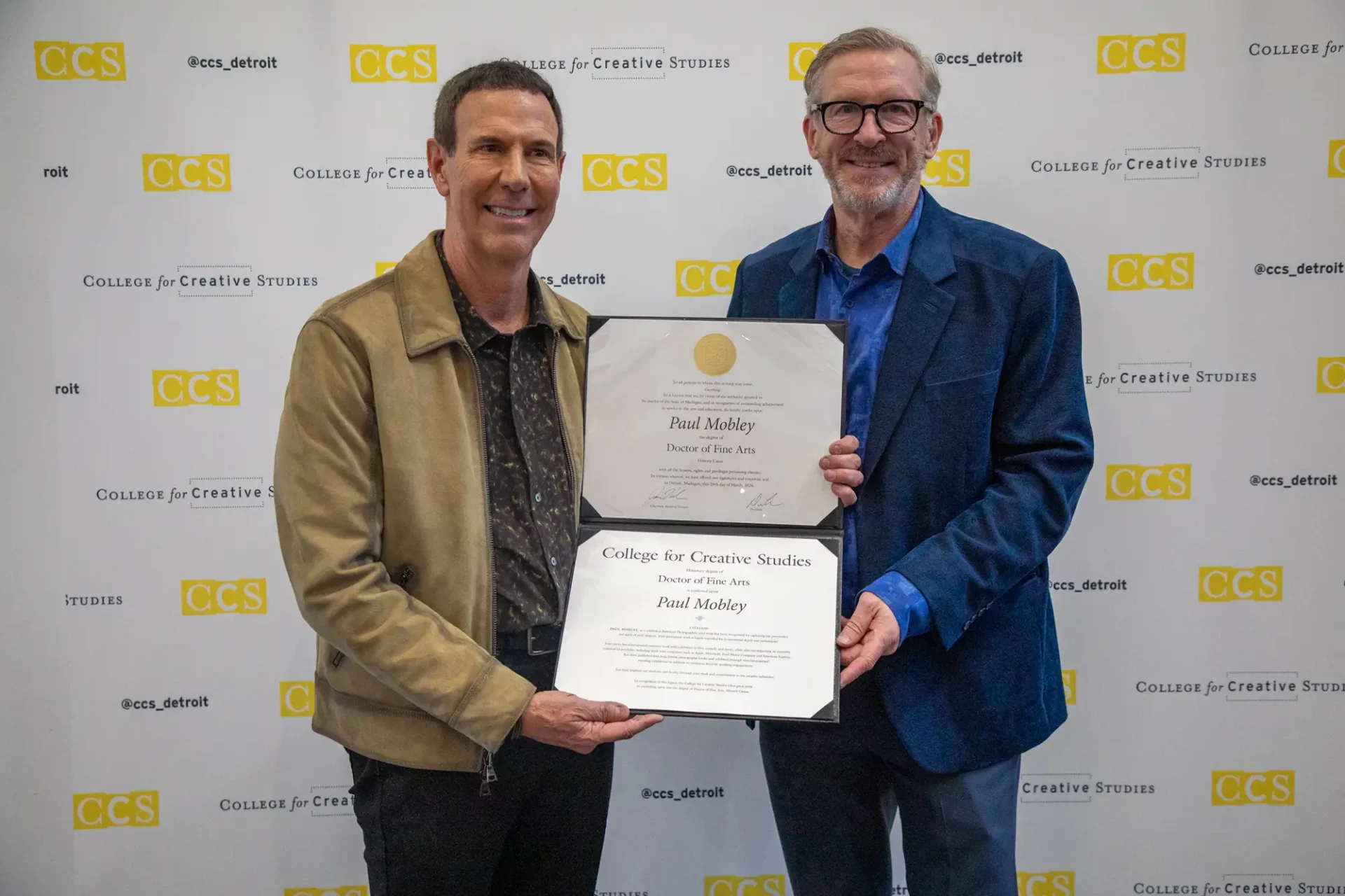 Paul Mobley on the left holding his Doctor of Fine Arts degree with President Don Tuski on the right.