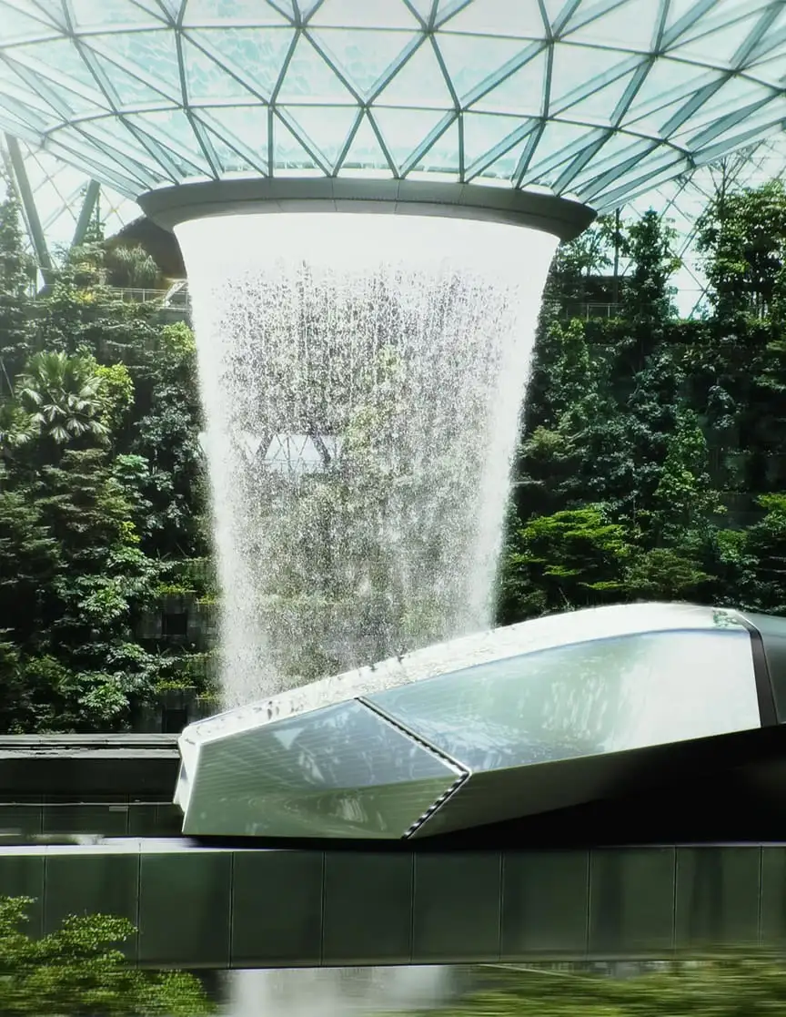 A vehicle in front of a large cascading water fall and lush greenery