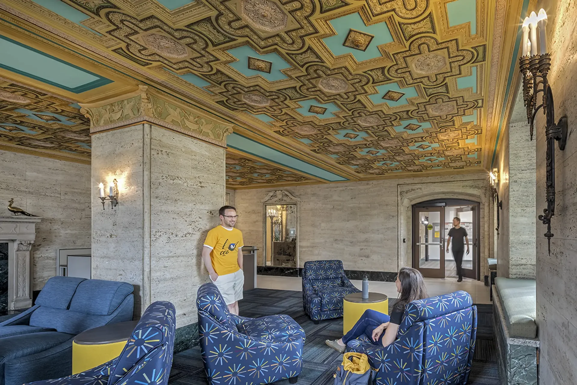 The lobby of the ACB. An intricate gold pattern adorns the ceiling; there are people in the seating area talking