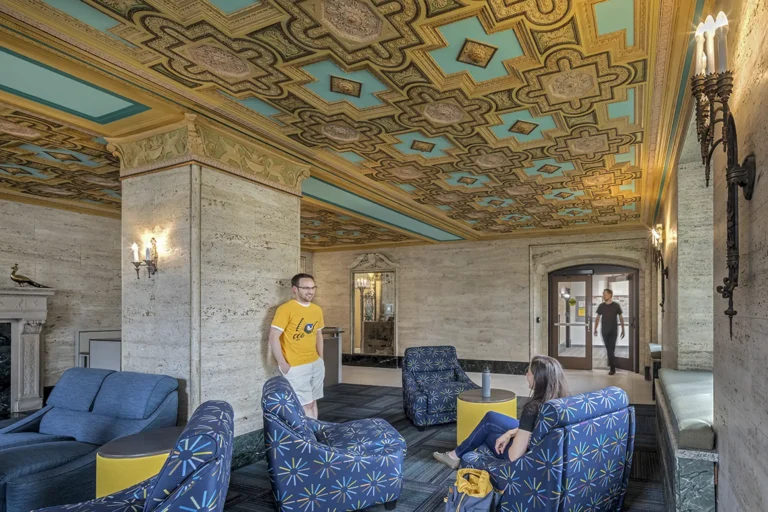 The lobby of the ACB. An intricate gold pattern adorns the ceiling; there are people in the seating area talking