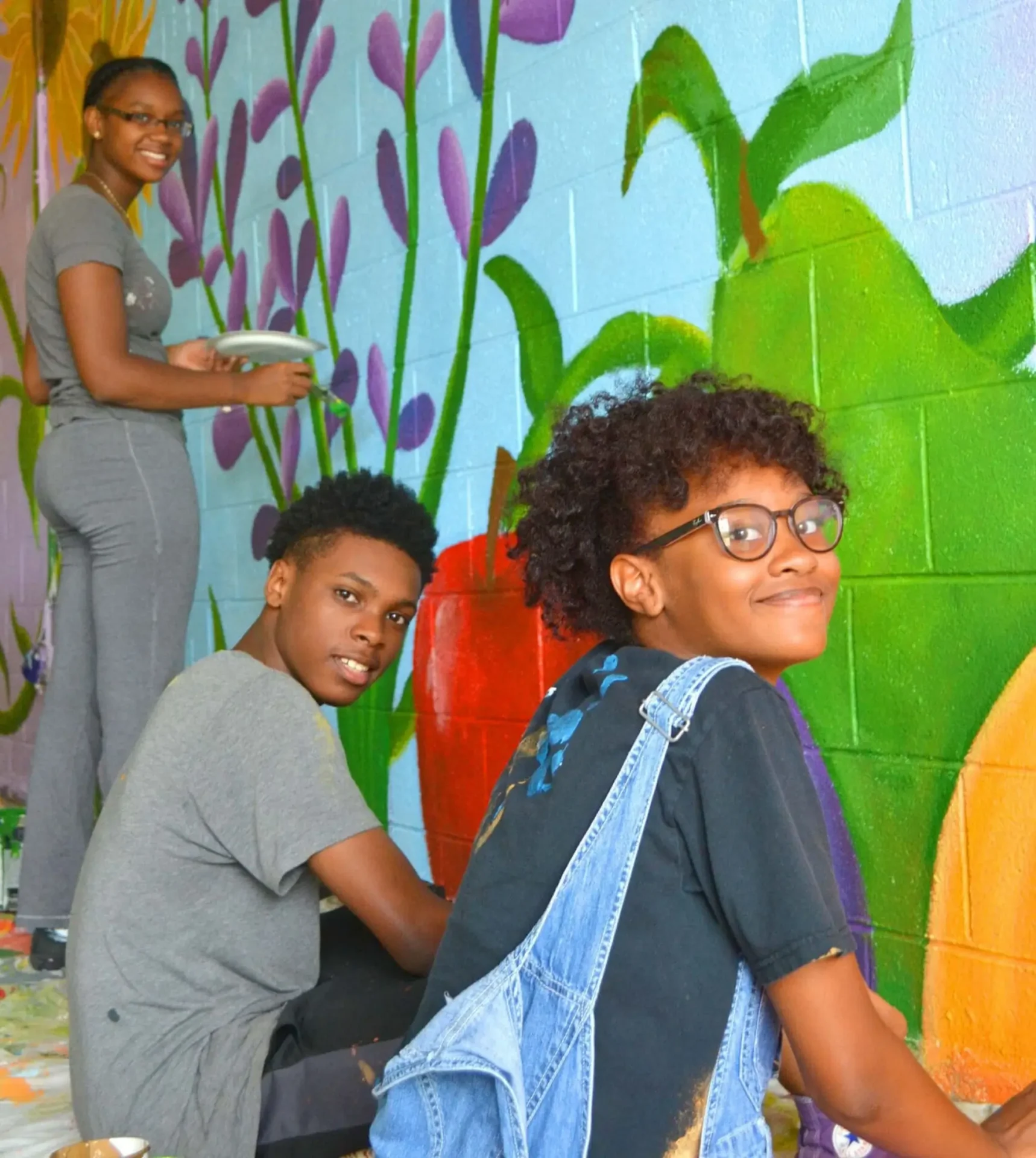 Students smiling in front of a mural they're working on
