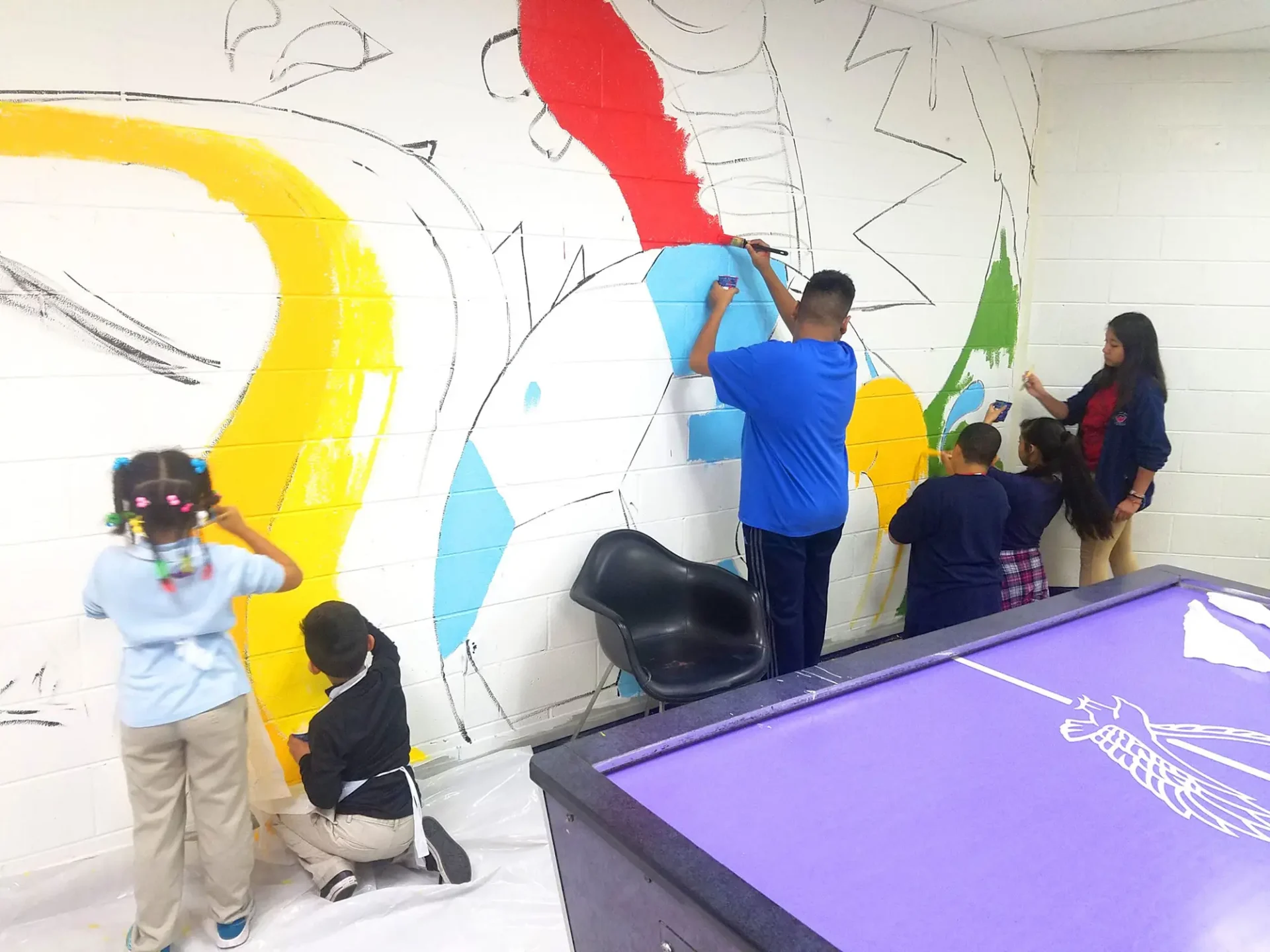 Students coloring and working on a wall mural inside a classroom