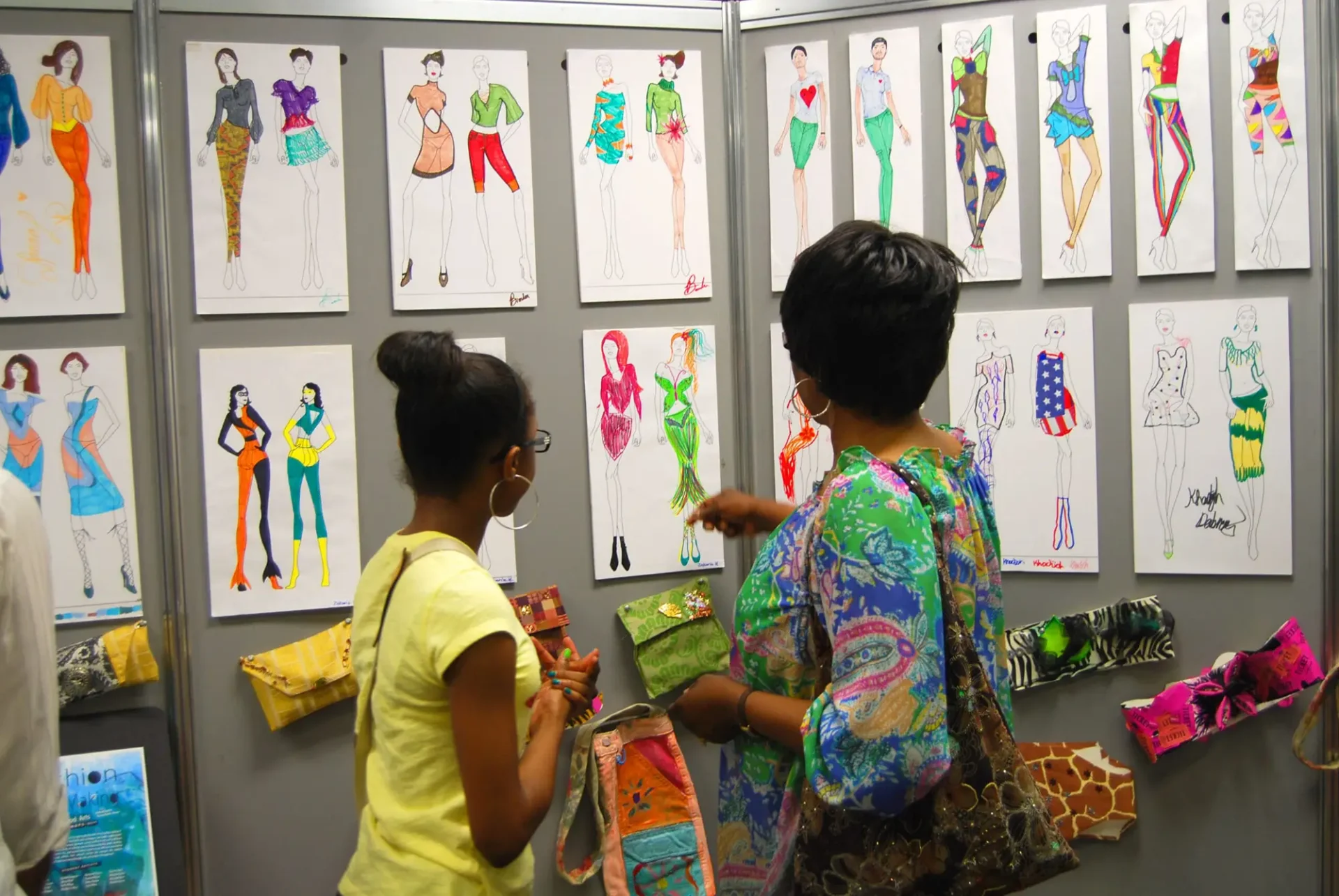 A woman and a young girl admiring a series of fashion sketches and drawings pinned on a board