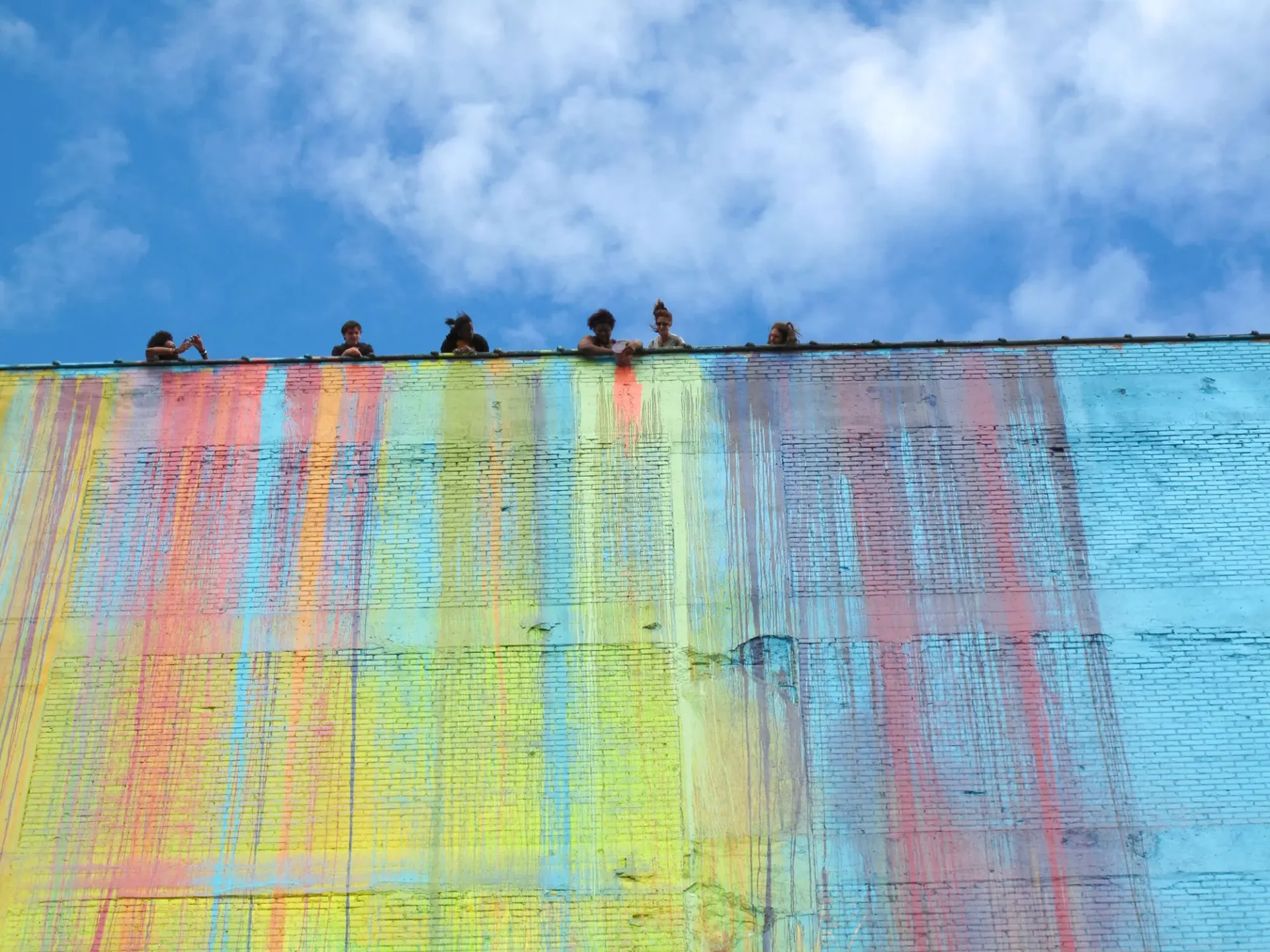 Students dumping buckets of paint down a brick wall to create a mural