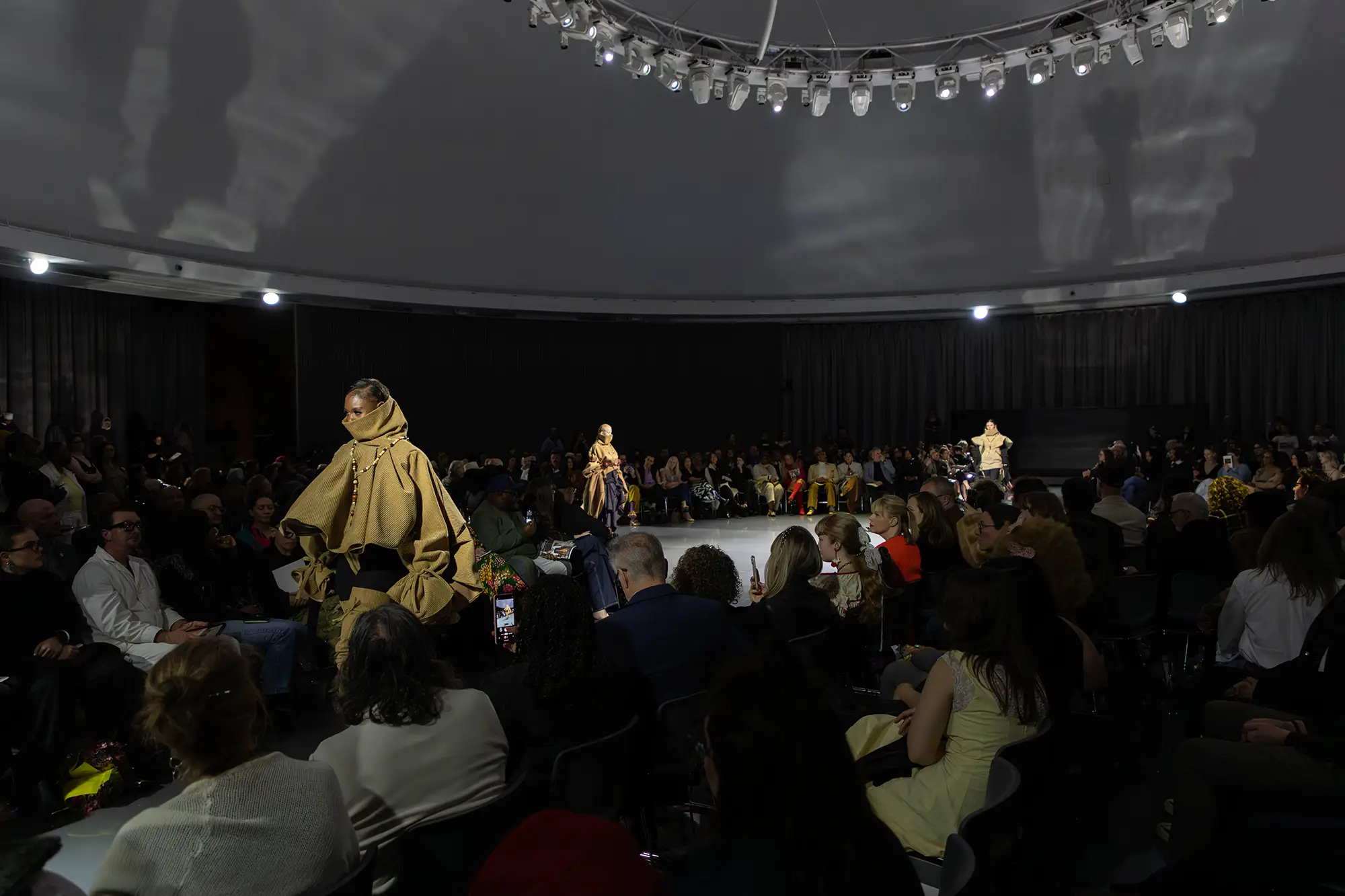 A dramatically lit scene of students showcasing their work on the catwalk at the Fashion Show