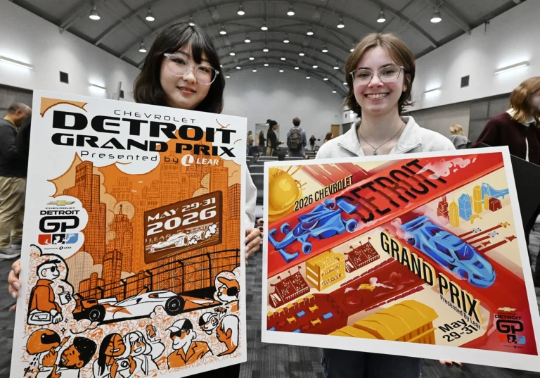 Two students holding up their poster designs for the Detroit Grand Prix