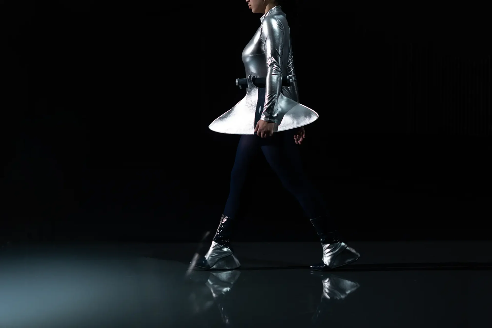 Model wearing a silver bodysuit with a silver bag and shoes
