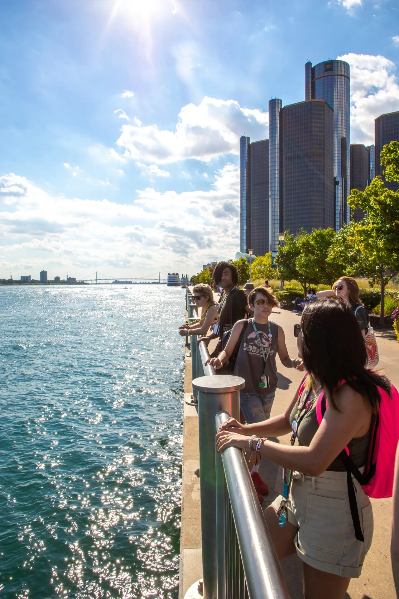 People looking out into the Detroit River on the river walk with the city behind them