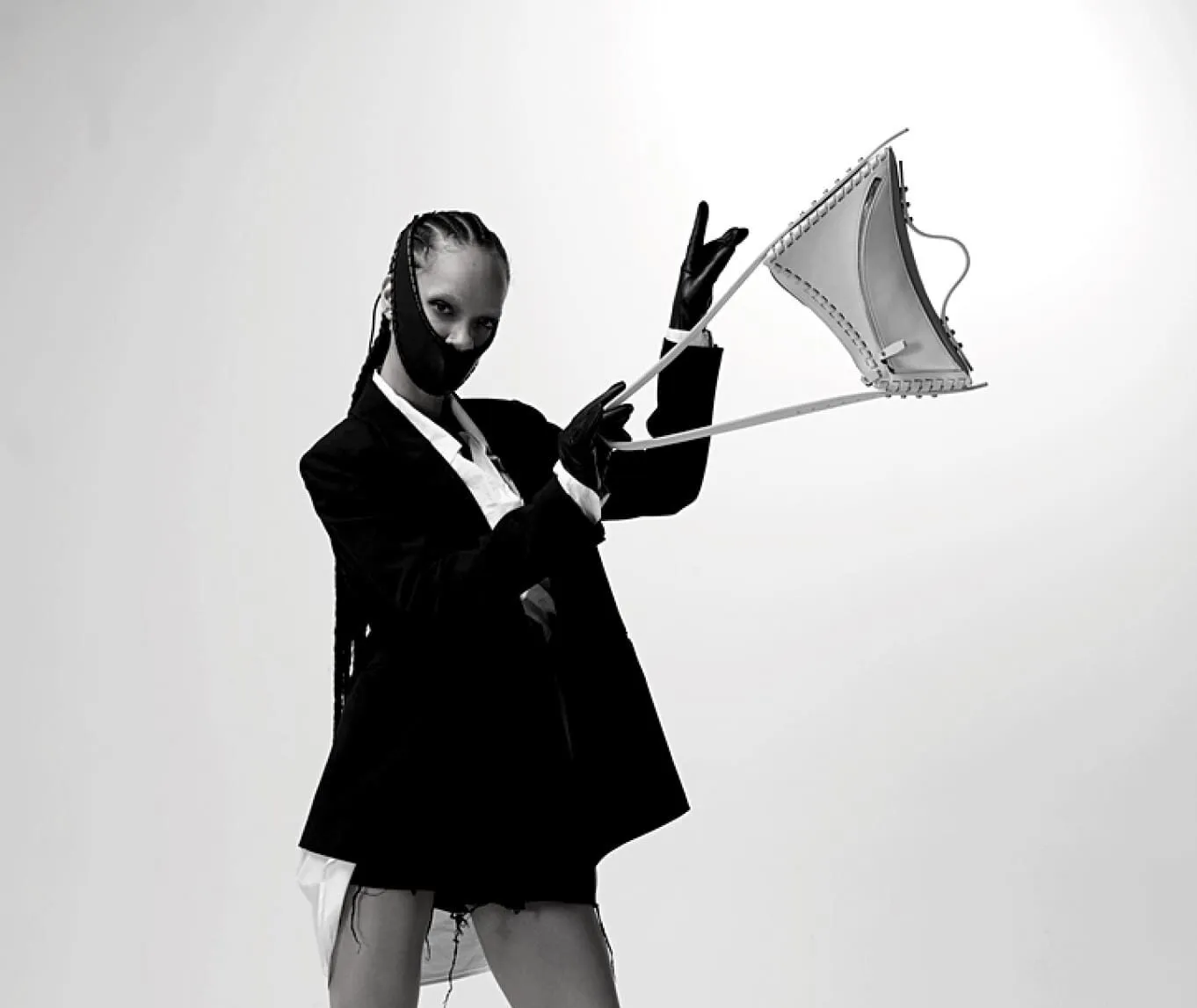 Black and white photograph of a model swinging a bag with grommets .