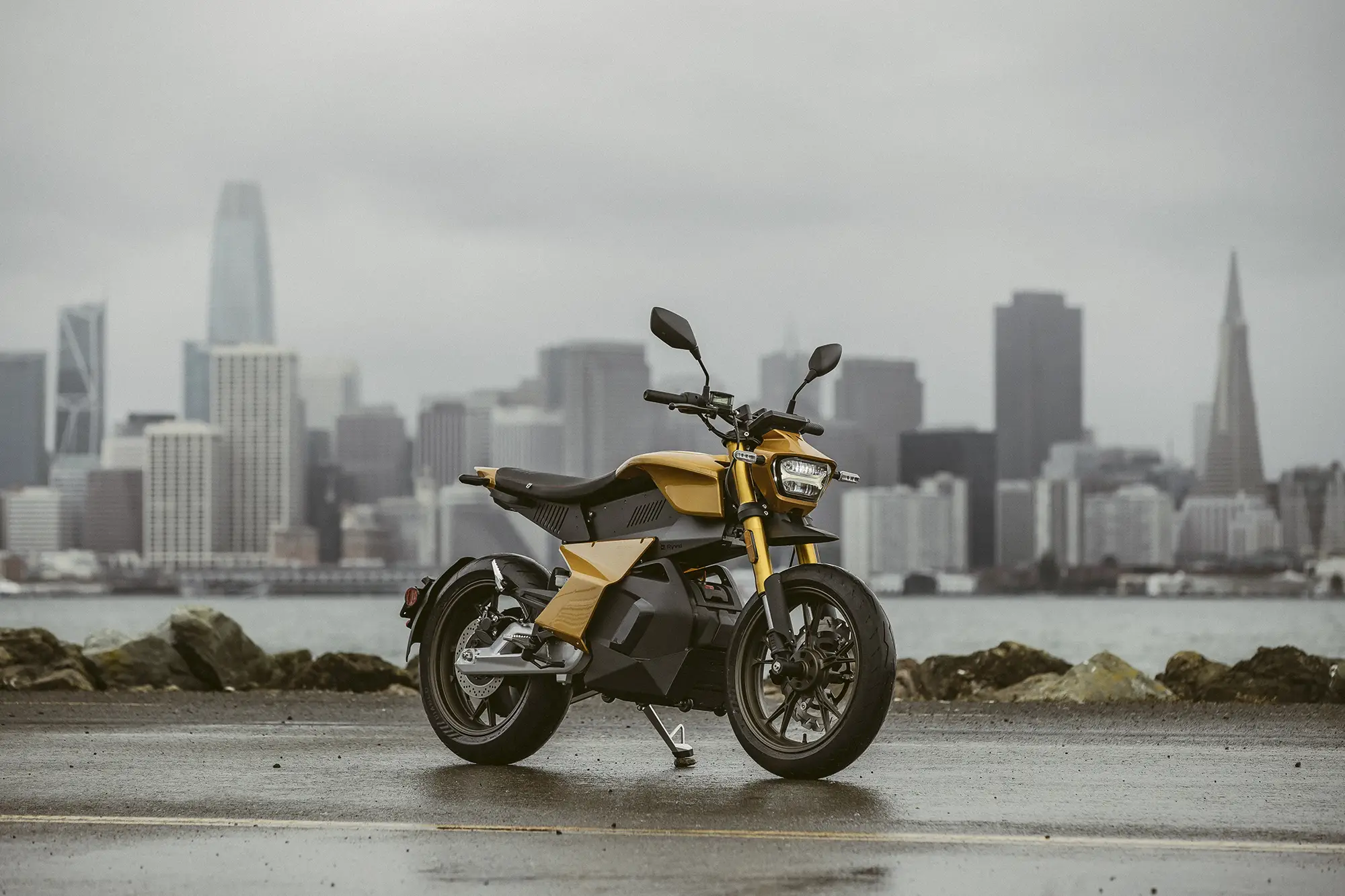 A motorcycle on a wet road with a river and cityscape in the background