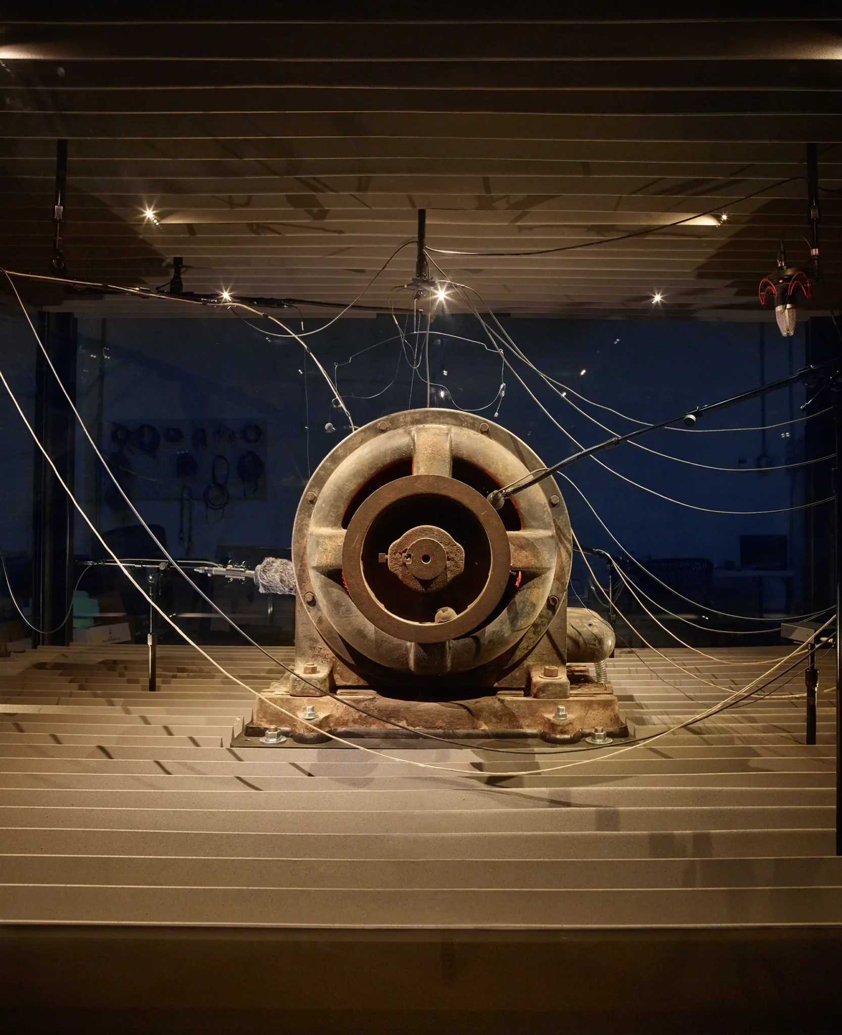 A giant circular structure, rusty in appearance, in a dimmly lit room with wires and pipes all around it