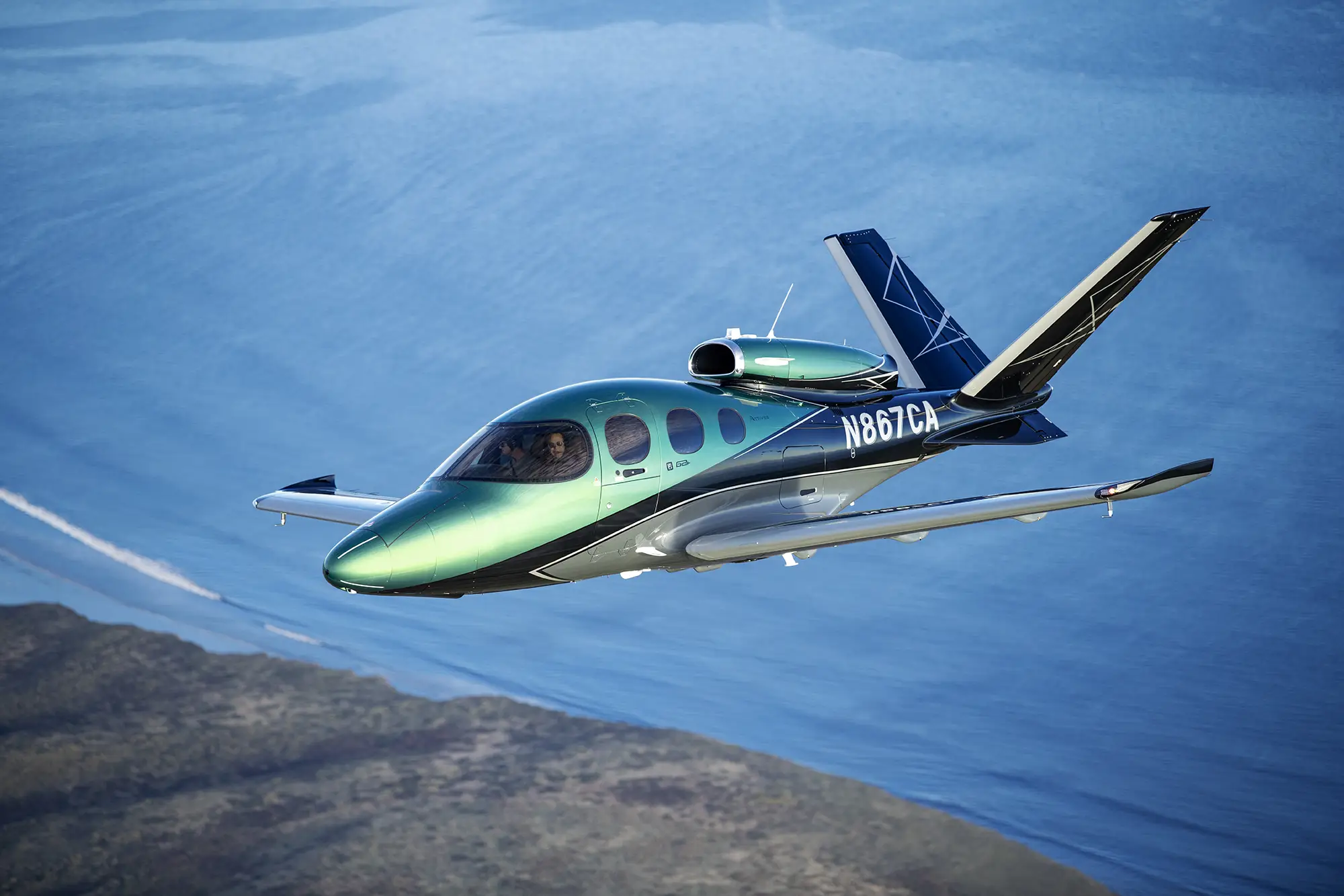 A plane flying over land and sea. It's tagged with N867CA on the side
