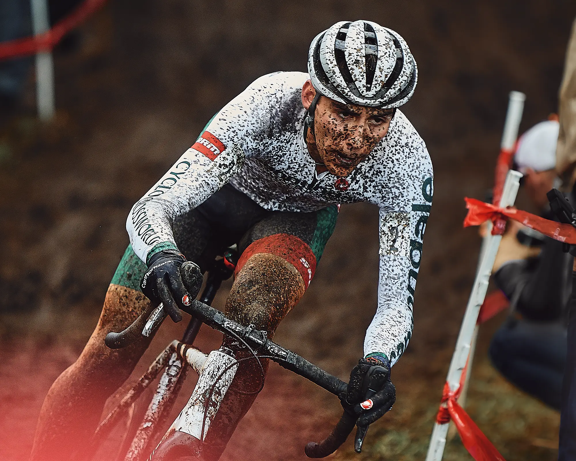 A cyclist in a white shirt, riding through the mud. The rider is splattered in mud