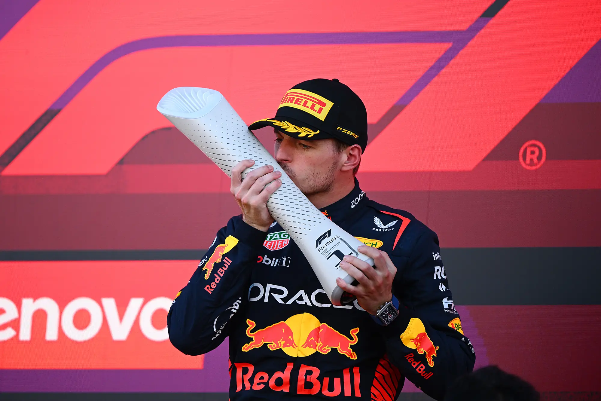 A racer holding up a white, cylindrical trophy, kissing it in front of a colorful background