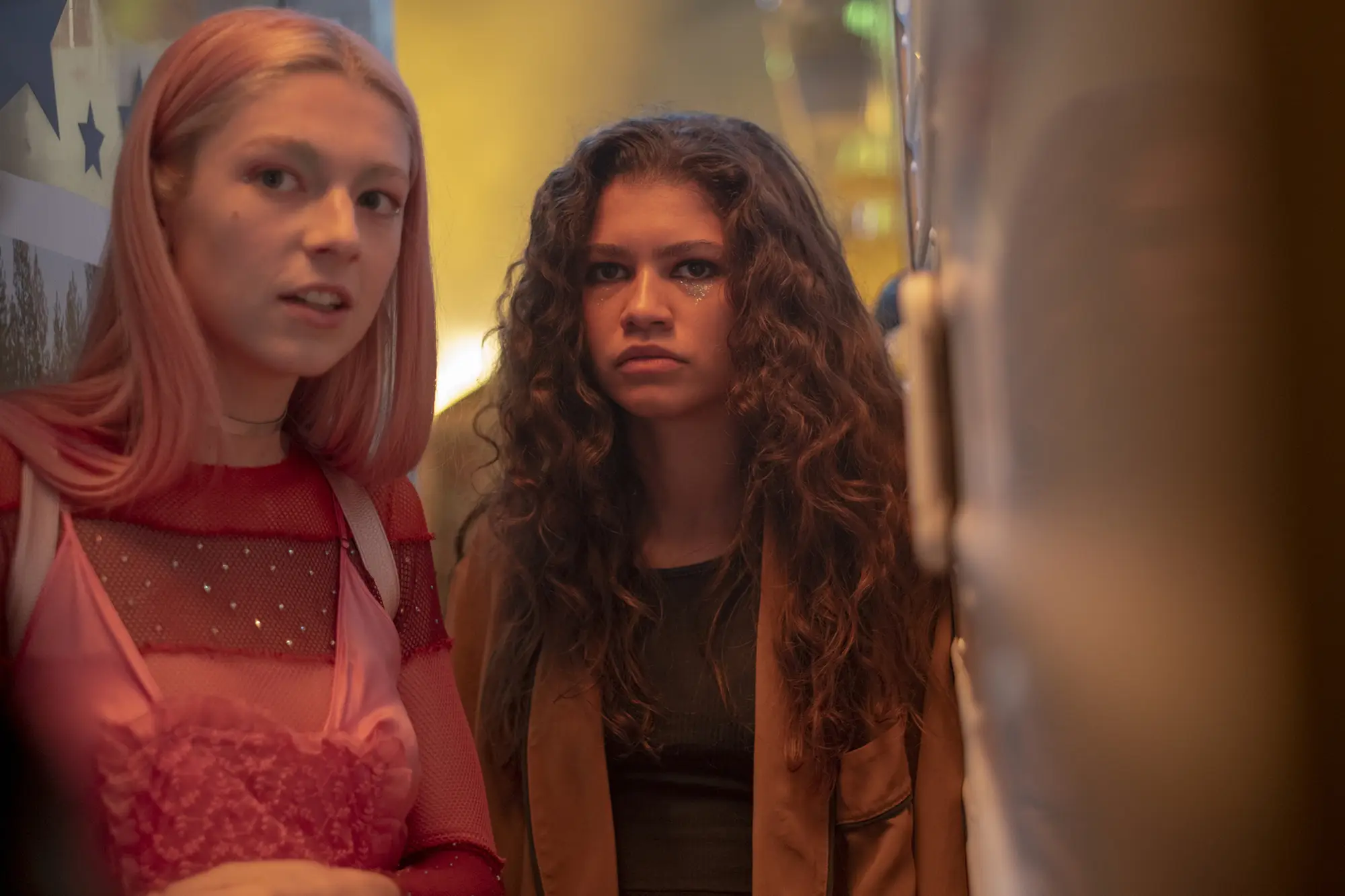 A scene of two young girls looking at the camera. They have glittery makeup under their eyes and are dressed fashionably