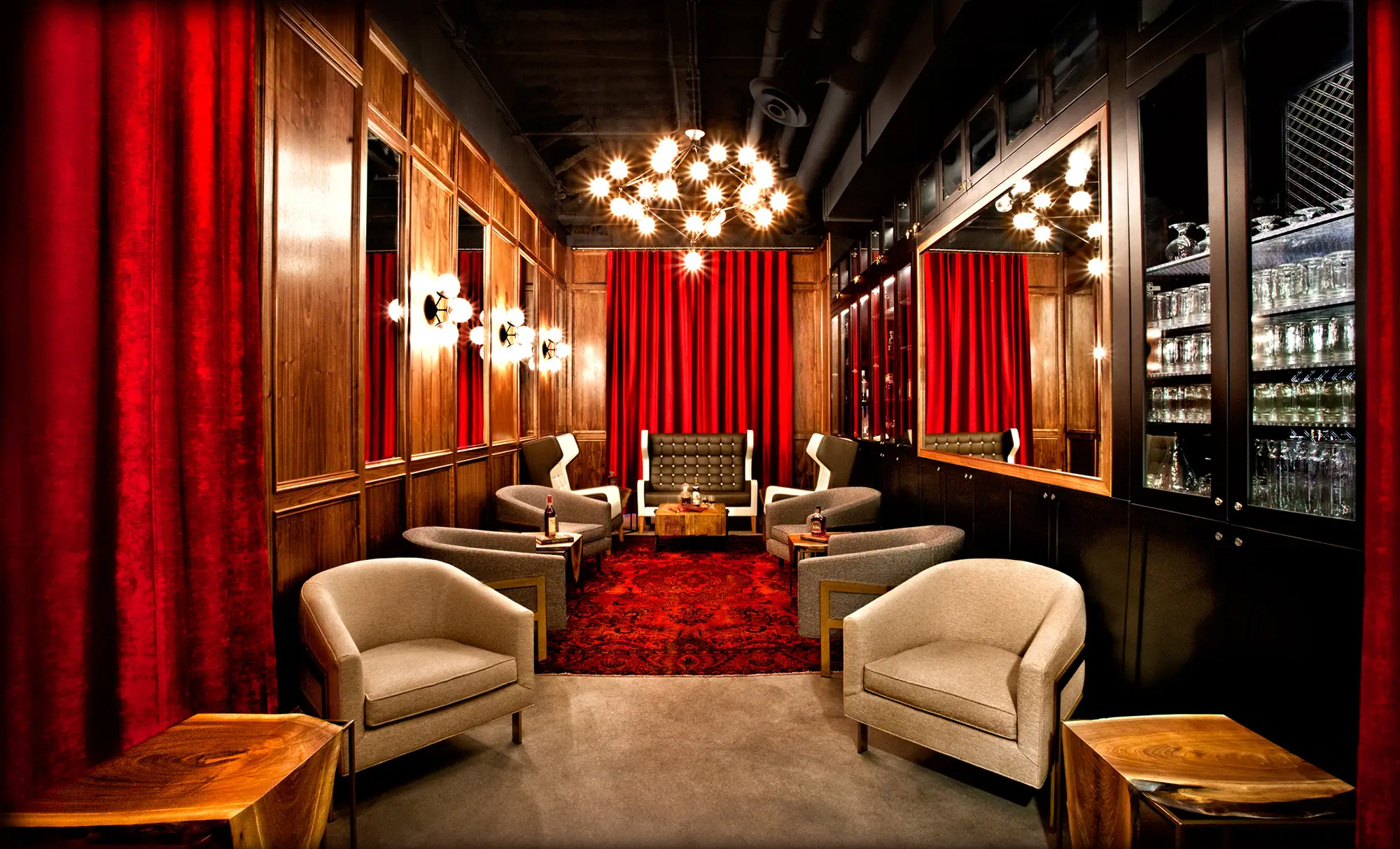 An elegant room, adorned with a bright red rug, 8 large chairs, decorative mirrors on the walls and a series of lights, chandeliers and sconces on the walls and ceiling, illuminating the room