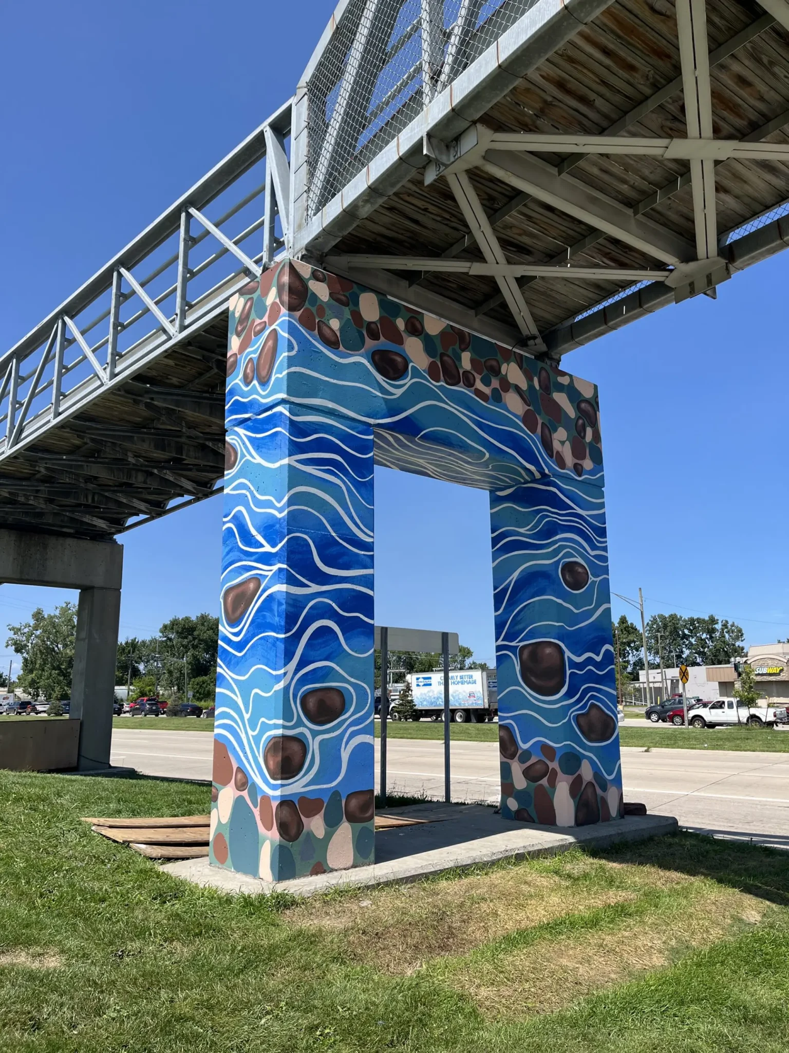 An image of an elevated walkway bridge that is painted with a water landscape and rocks