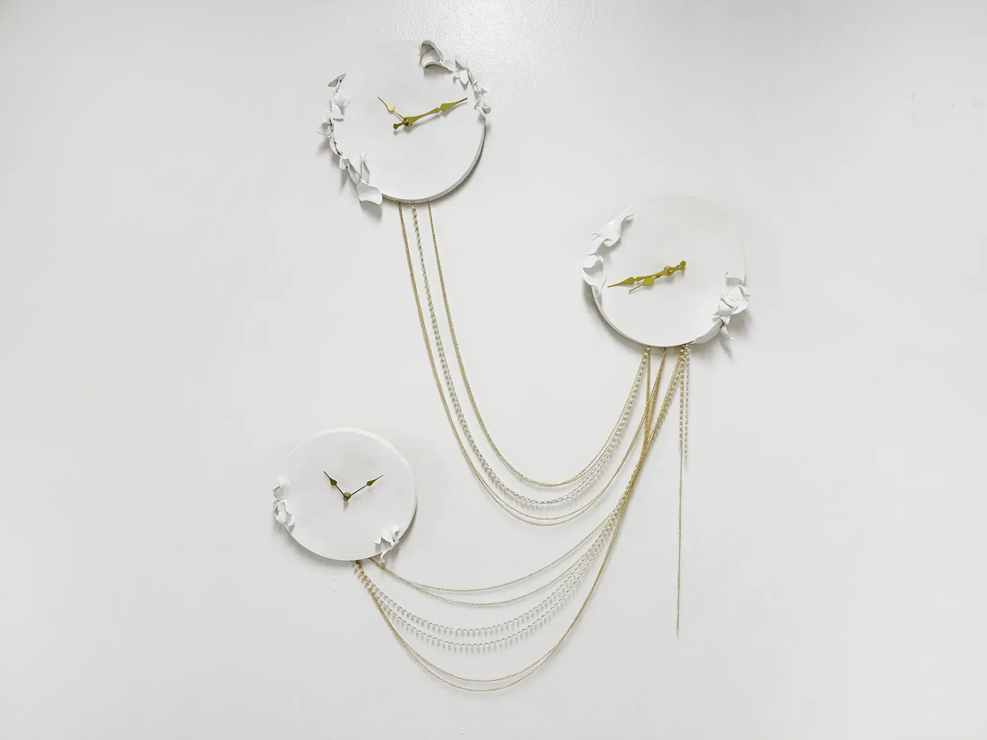 3 white clocks connected to each other by gold chains.