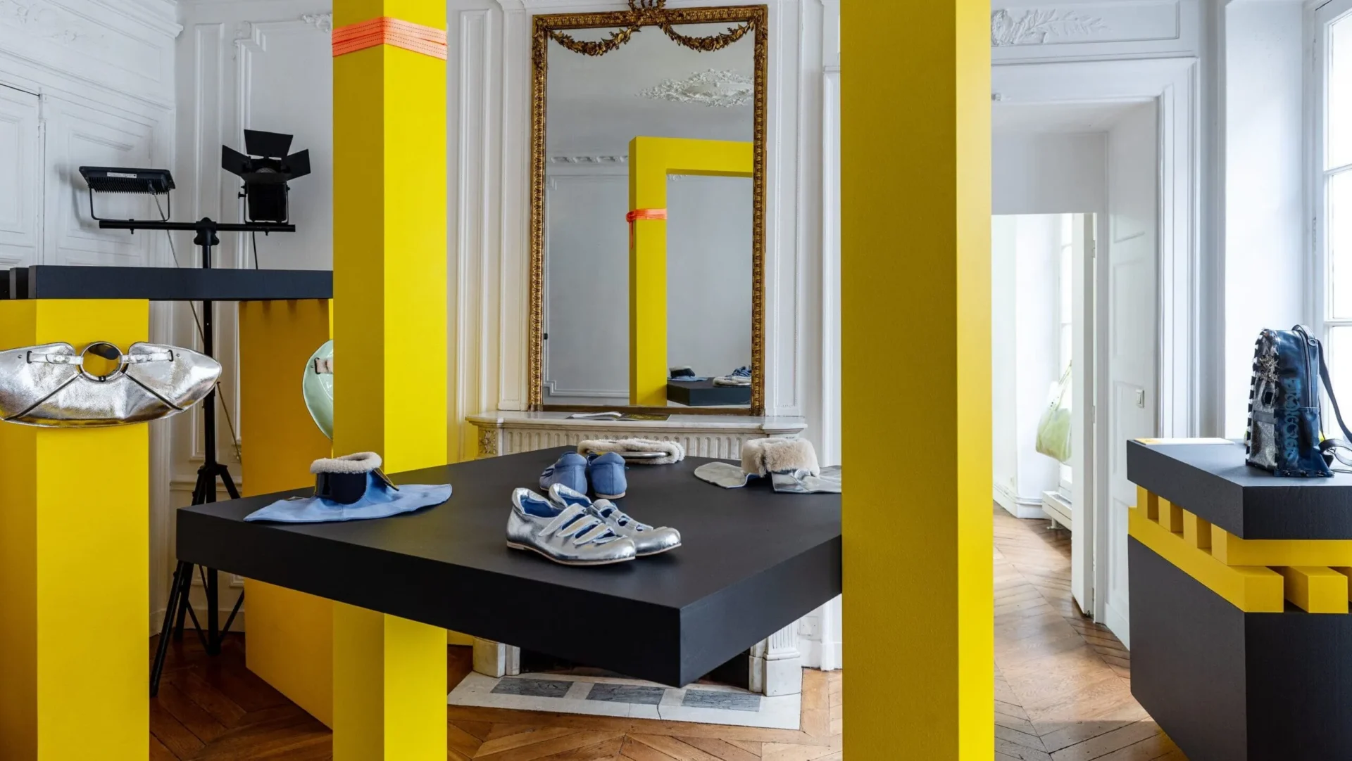 A white showroom with yellow columns displaying handbags, shoes and accessories designed by CCS students at Paris Fashion Week.