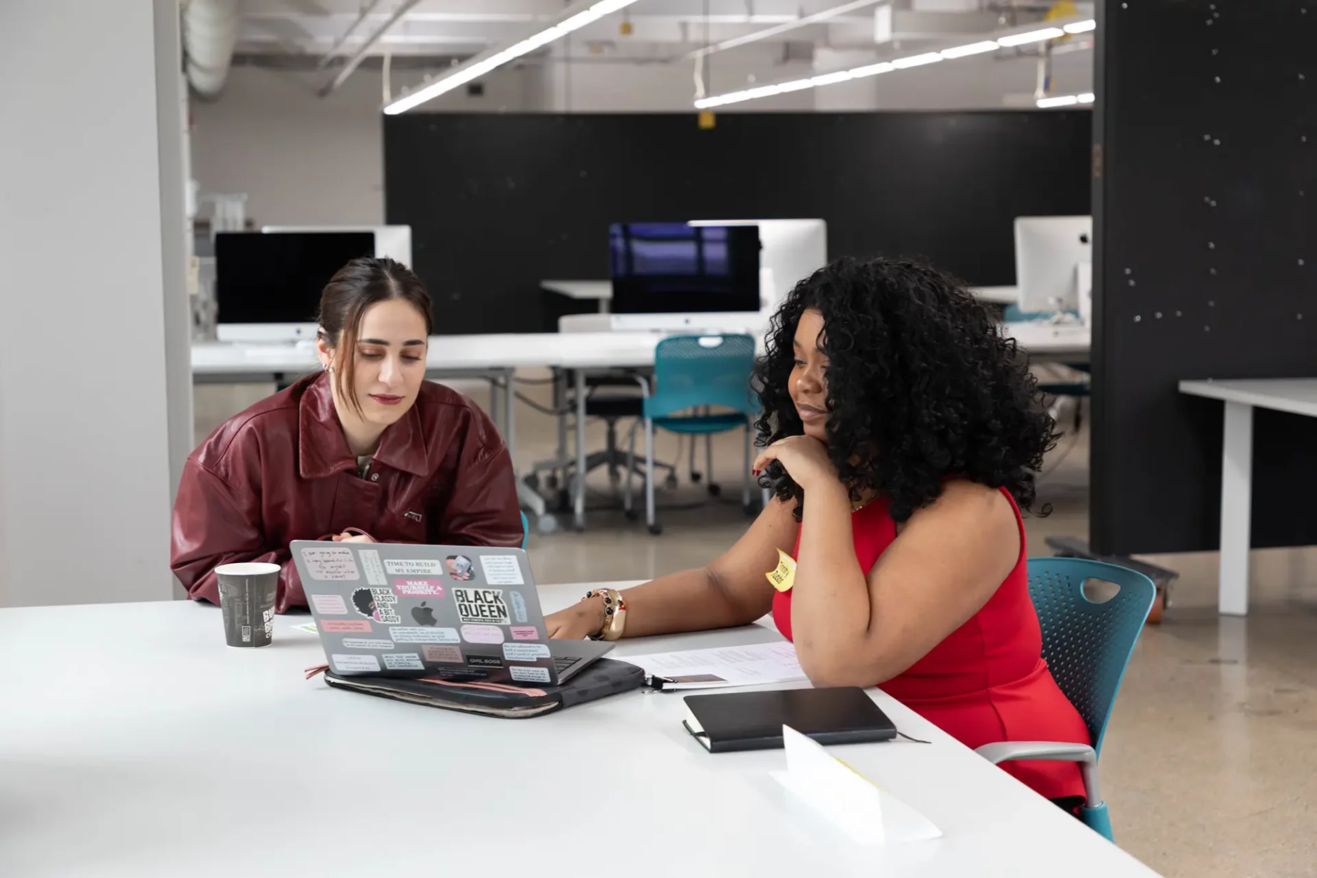 Two students working together at a table on a laptop