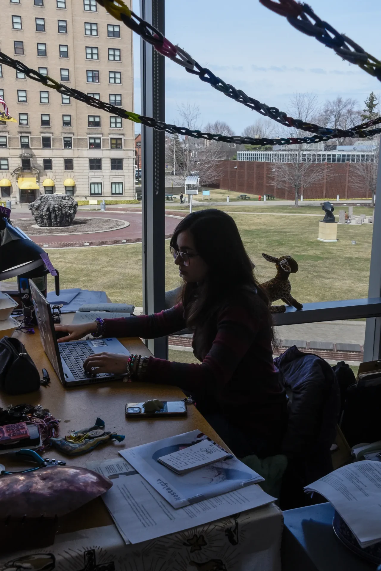 A student working on a laptop in front of a window overlooking the Ford campus