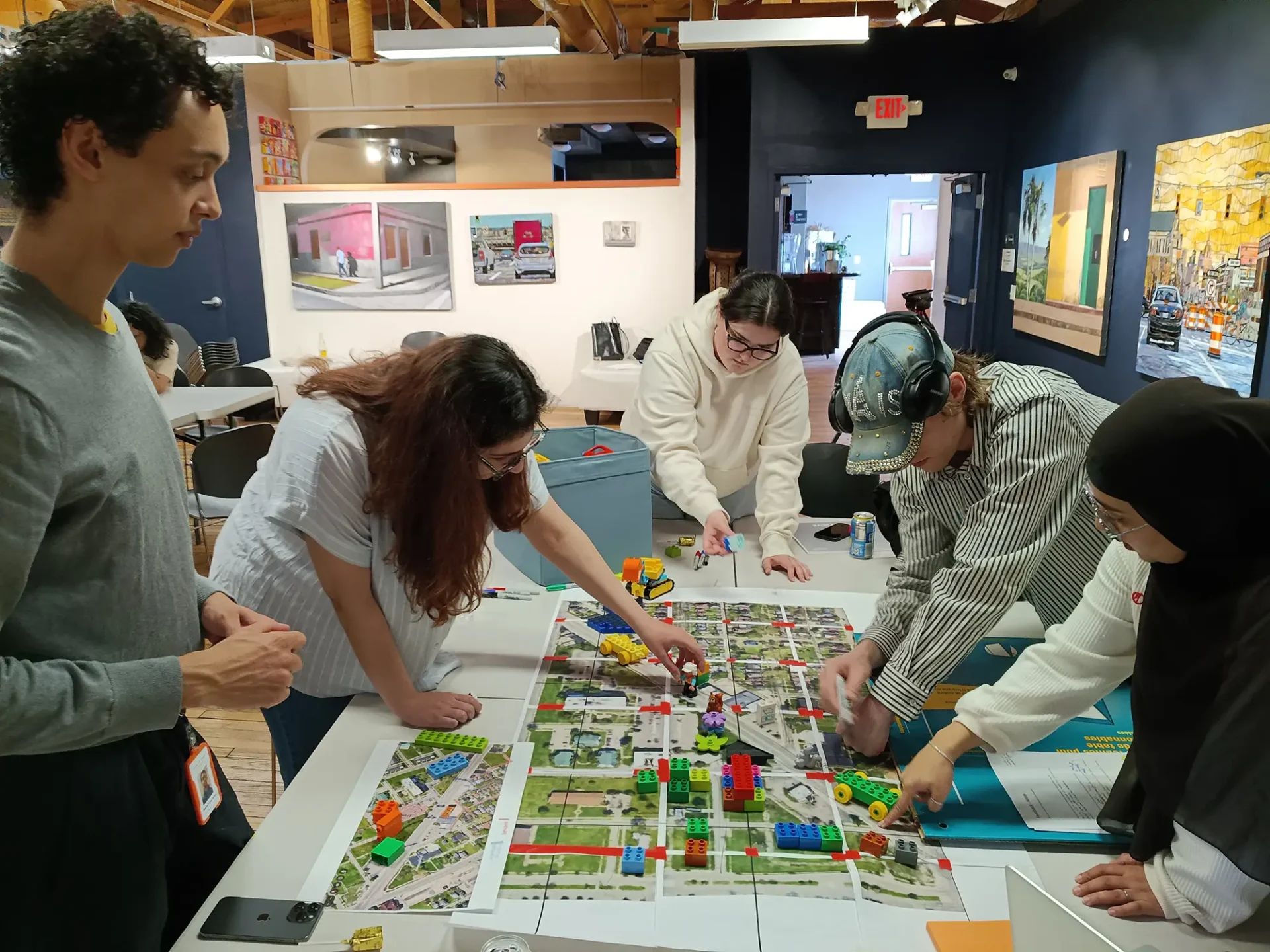 A group of students laying large lego blocks on top of a map on a table surrounded by artwork in the background