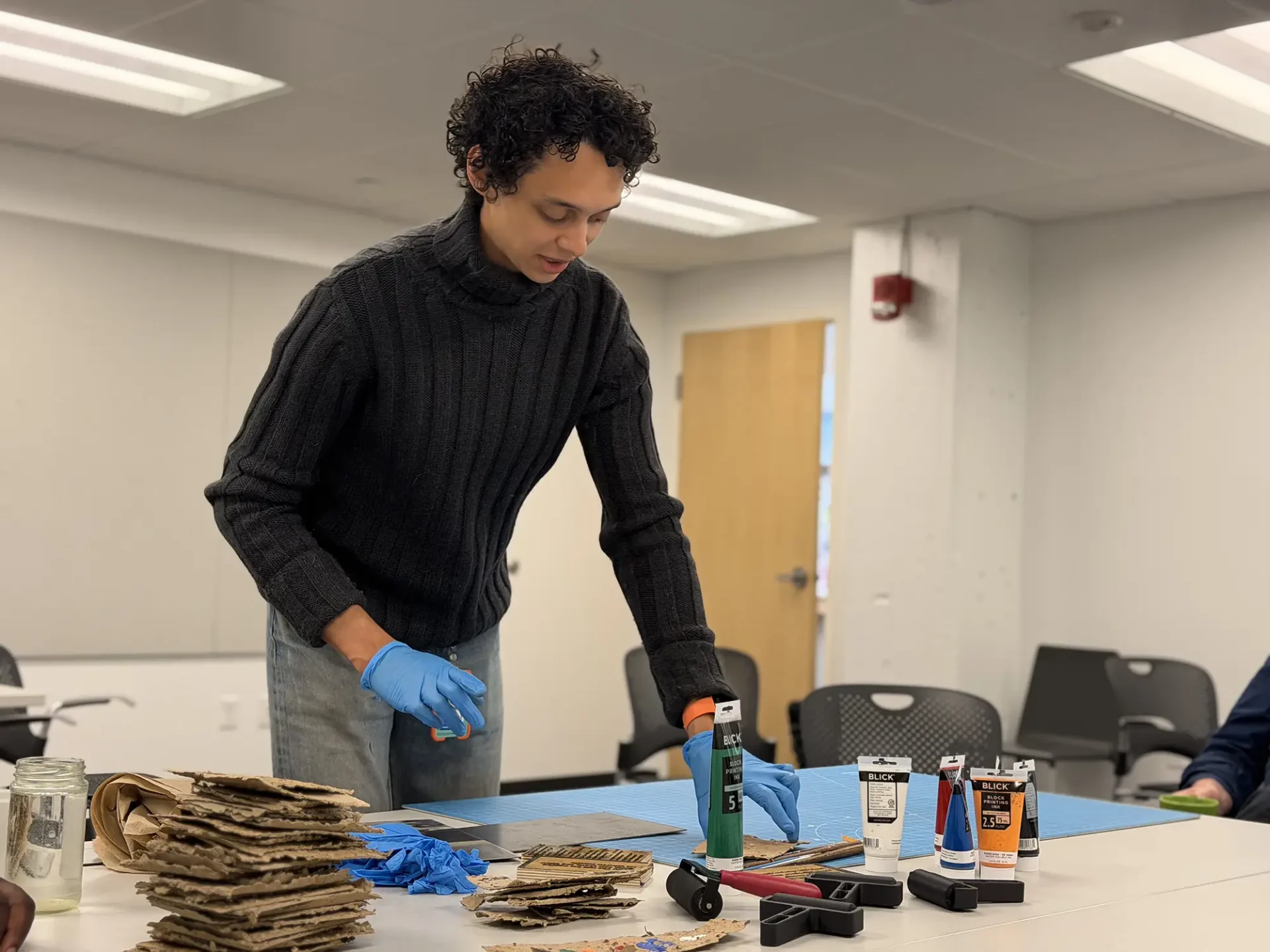 A student laying out their work on a board at a table. The student is wearing blue gloves