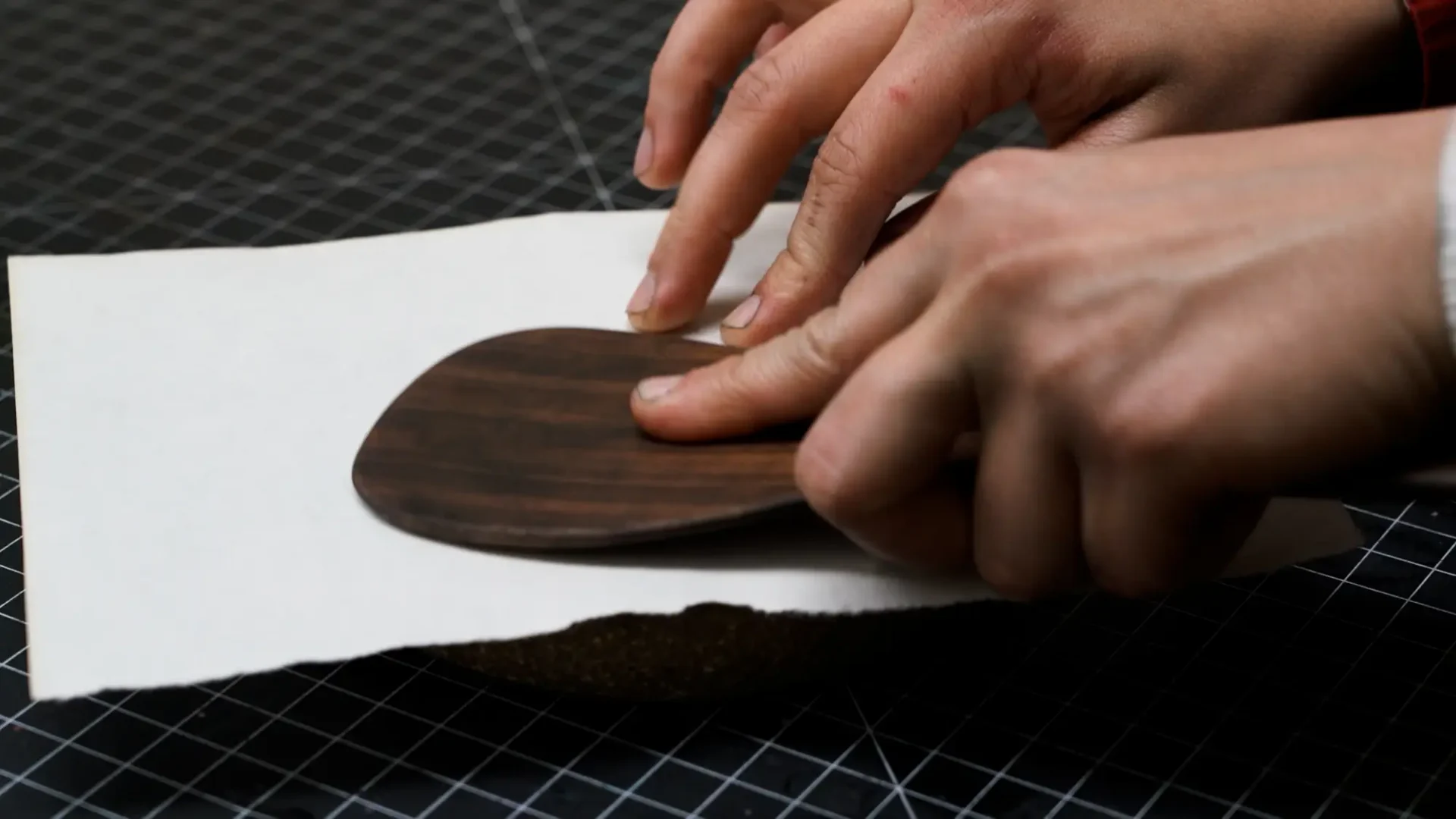 Film still from thesis process film; close-up of hands and brayer printing from ceramic plate