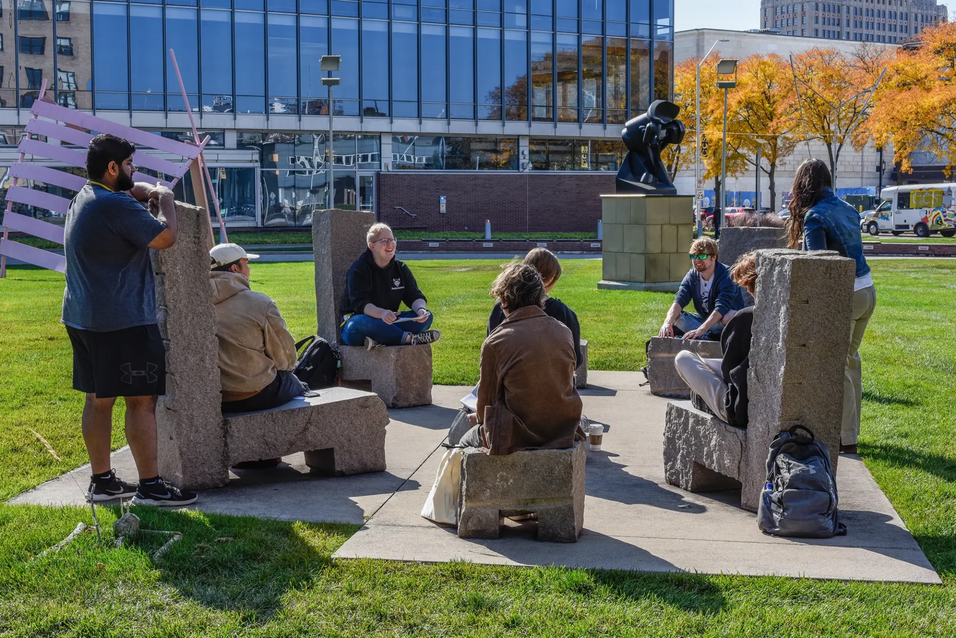 A group of students gathered in a circle, sitting in large stone chairs in the sculpture garden on the Ford campus