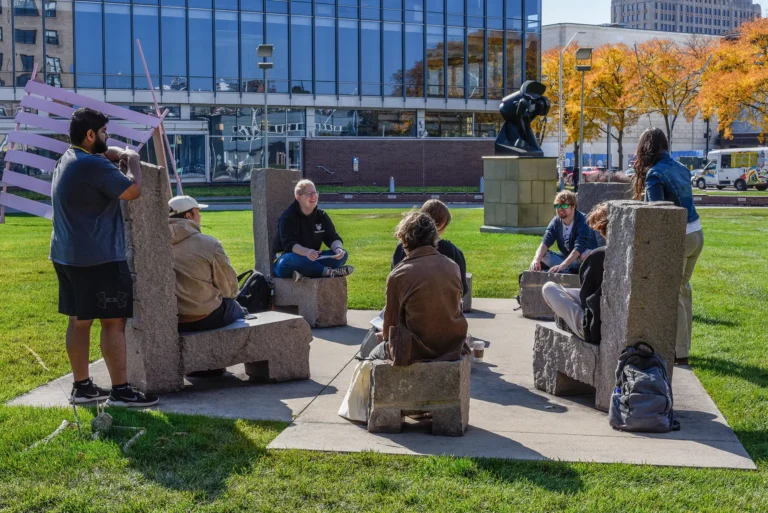 A group of students gathered in a circle, sitting in large stone chairs in the sculpture garden on the Ford campus