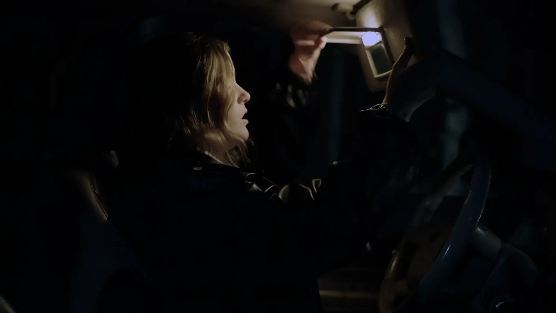 Profile shot of a woman checking her face in the visor of a car at night.