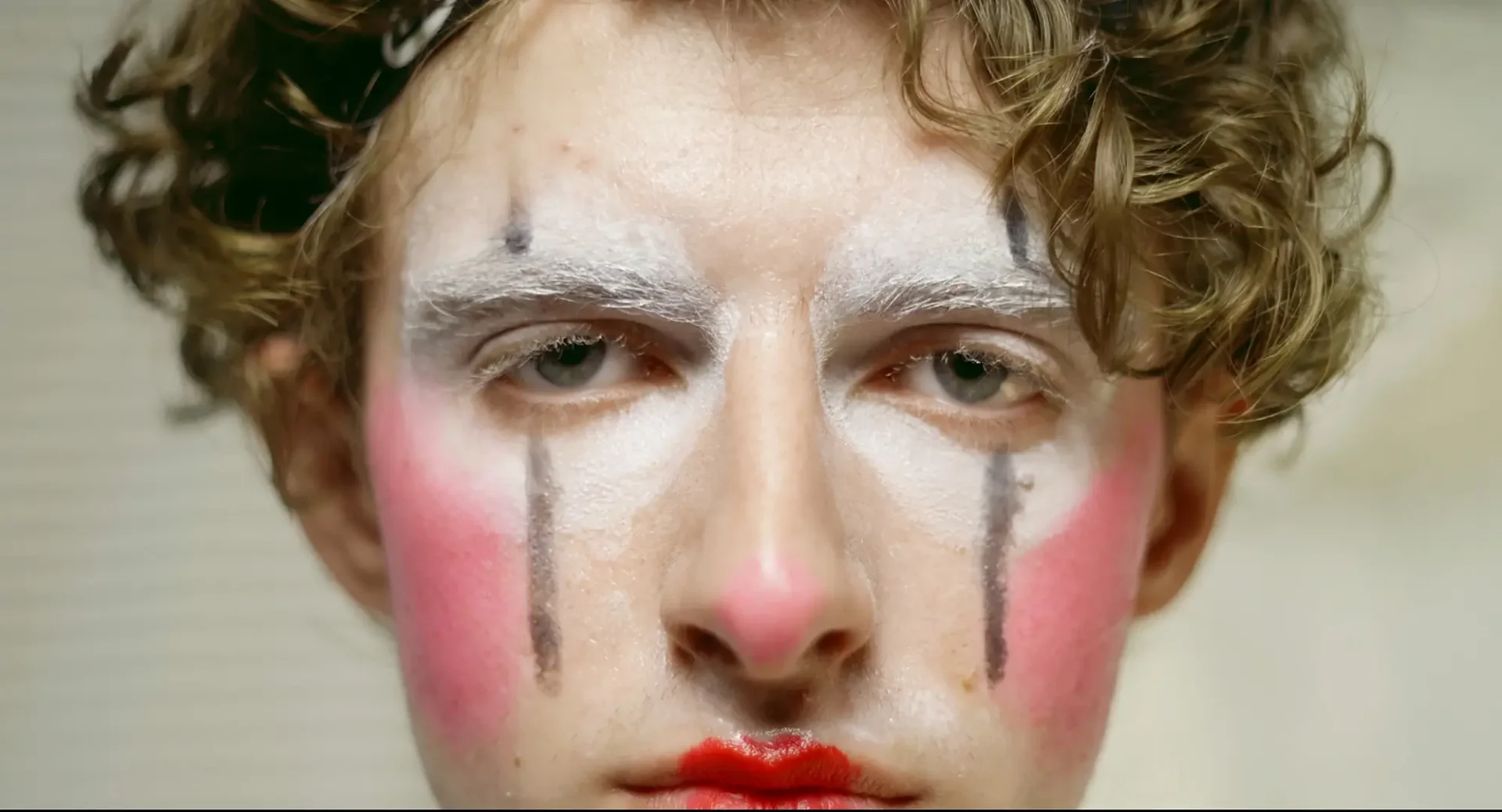 Film still: close-up of a young man in clown makeup.