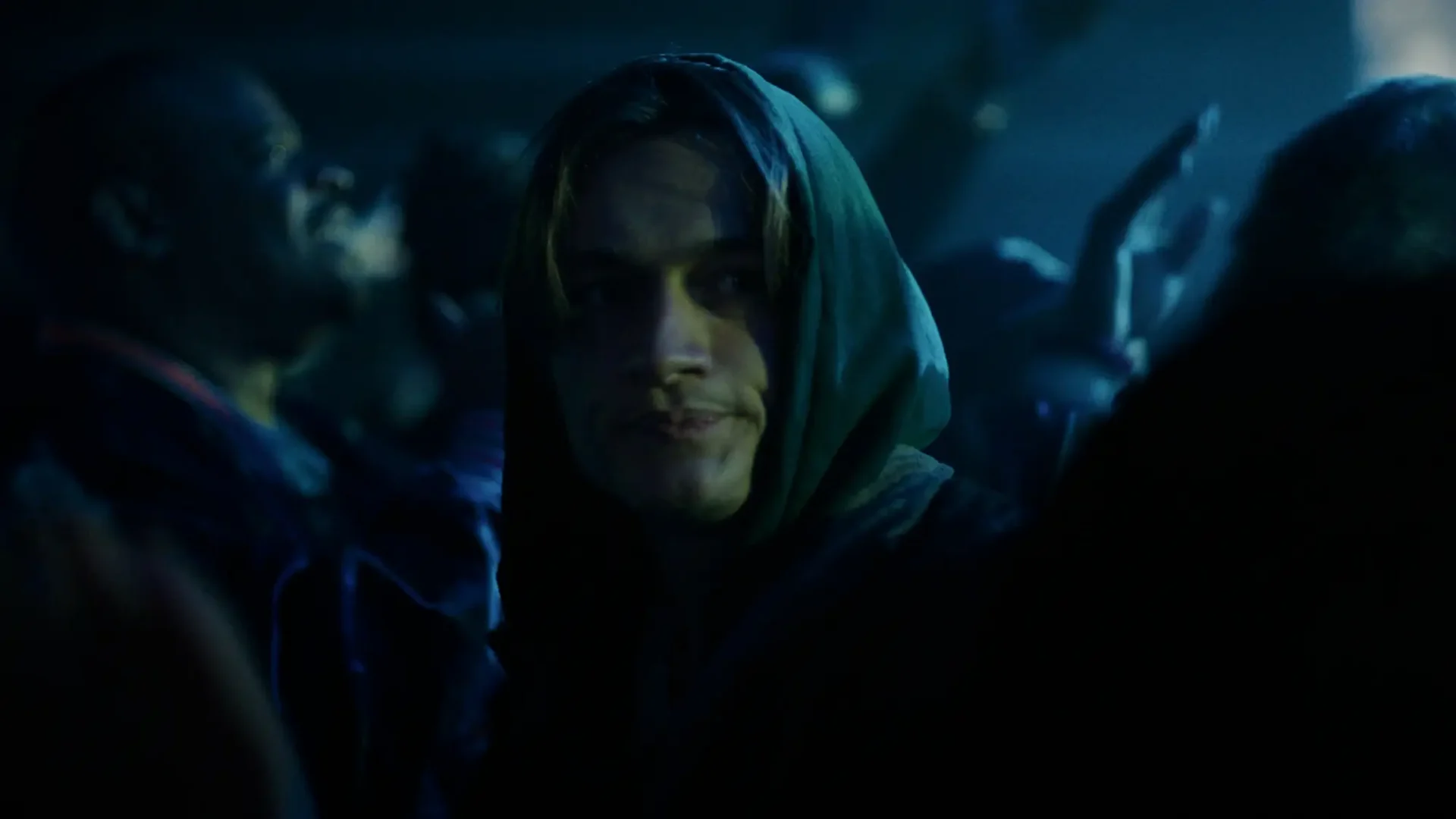 Film still from 2K thriller Random Bathrooms: Medium shot of a young man in hoodie looking across a crowded dance floor.