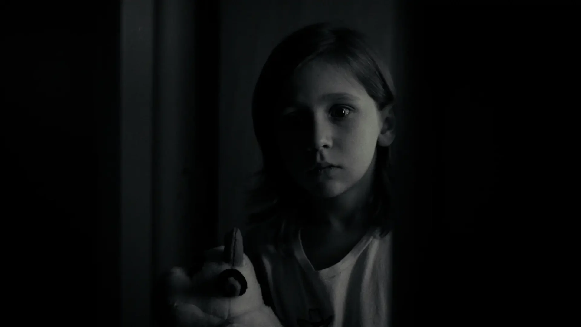 Film still from 2K thriller Random Bathrooms, a lack and white flashbook: medium-close shot of young boy holding a stuffed animal watching something happen off camera.
