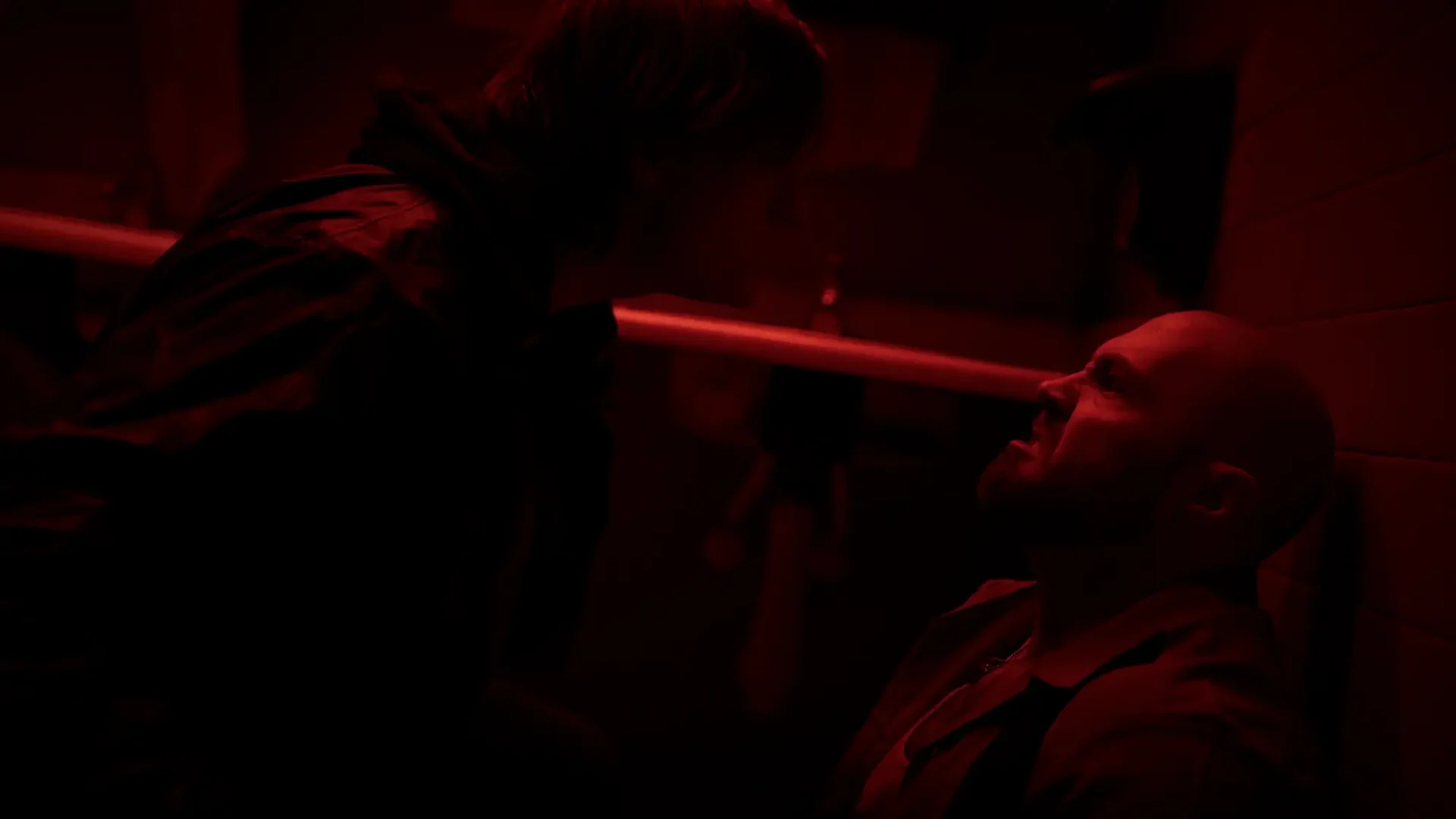 Film still from 2K thriller Random Bathrooms: Red-tinted two-shot of a young man confronting his slightly older aggressor in the bathroom.