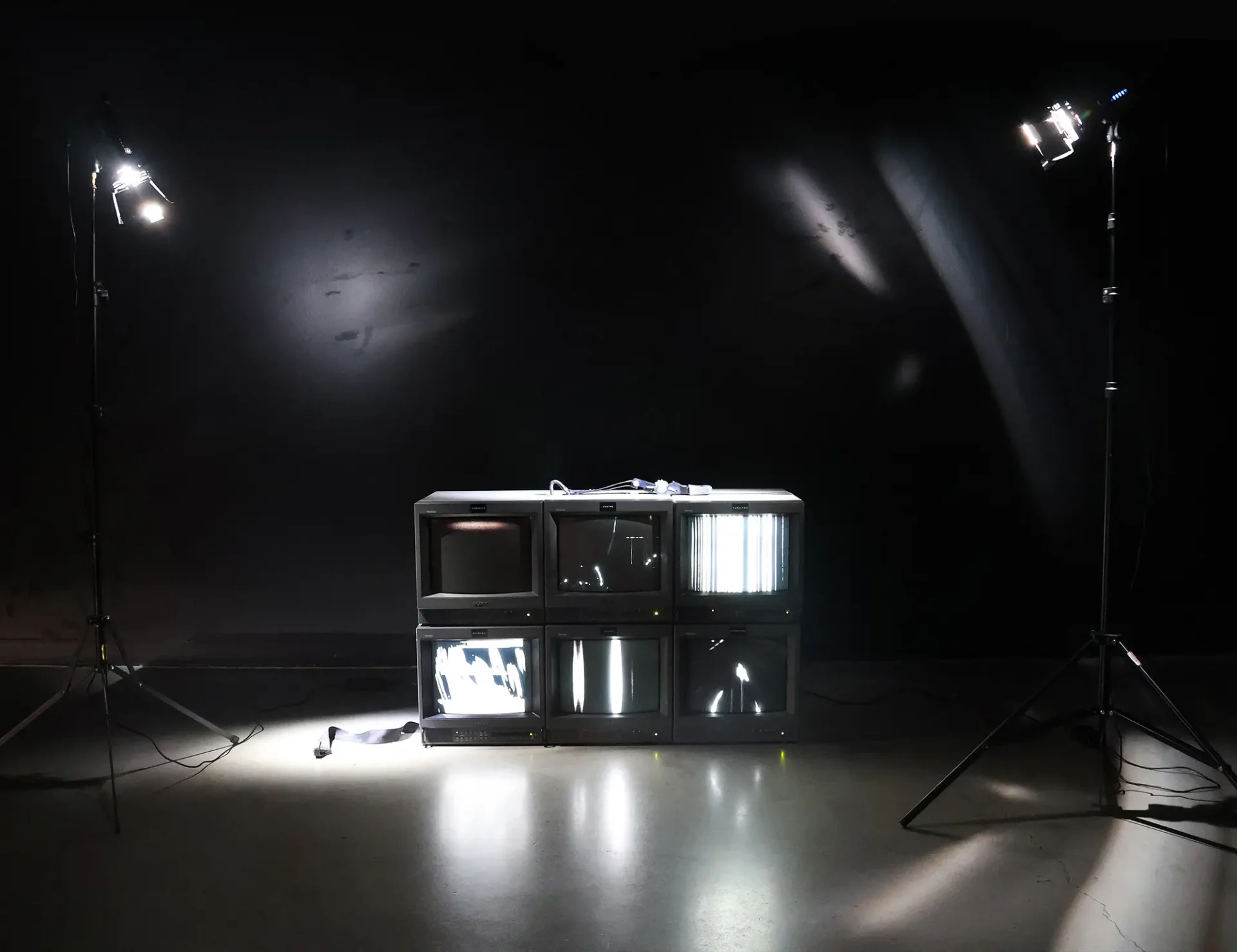 Documentation of 6-channel video installation: 6 CRTs are stacked in 2 rows with 6 unique, black and white glitch videos. The TVs are strapped together and show with stage lighting to emphasize the bindings and cords.