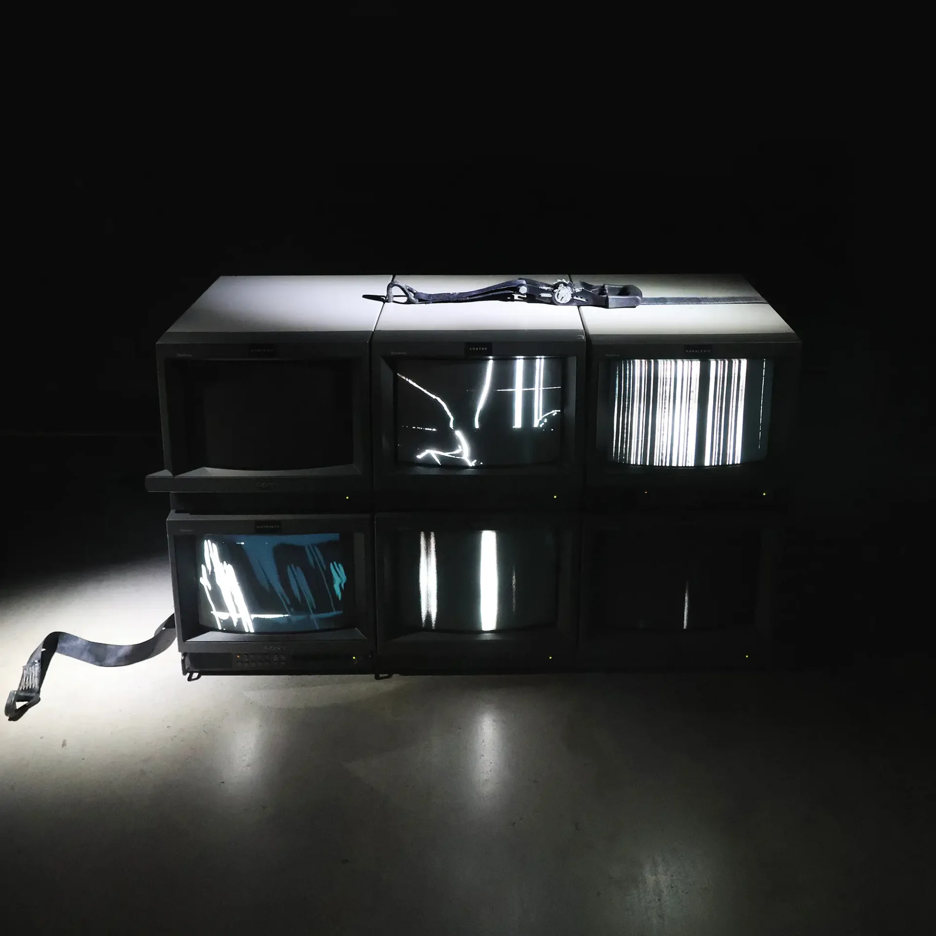 Documentation of 6-channel video installation: 6 CRTs are stacked in 2 rows with 6 unique, black and white glitch videos. The TVs are strapped together and shown with stage lighting to emphasize the bindings and cords.