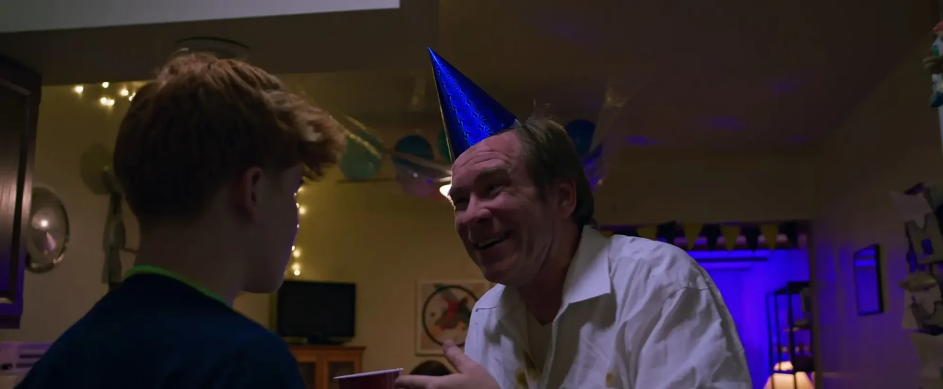 Film still from narrative short New Year: An older man in a party hat talks to a boy at the New Year's party.