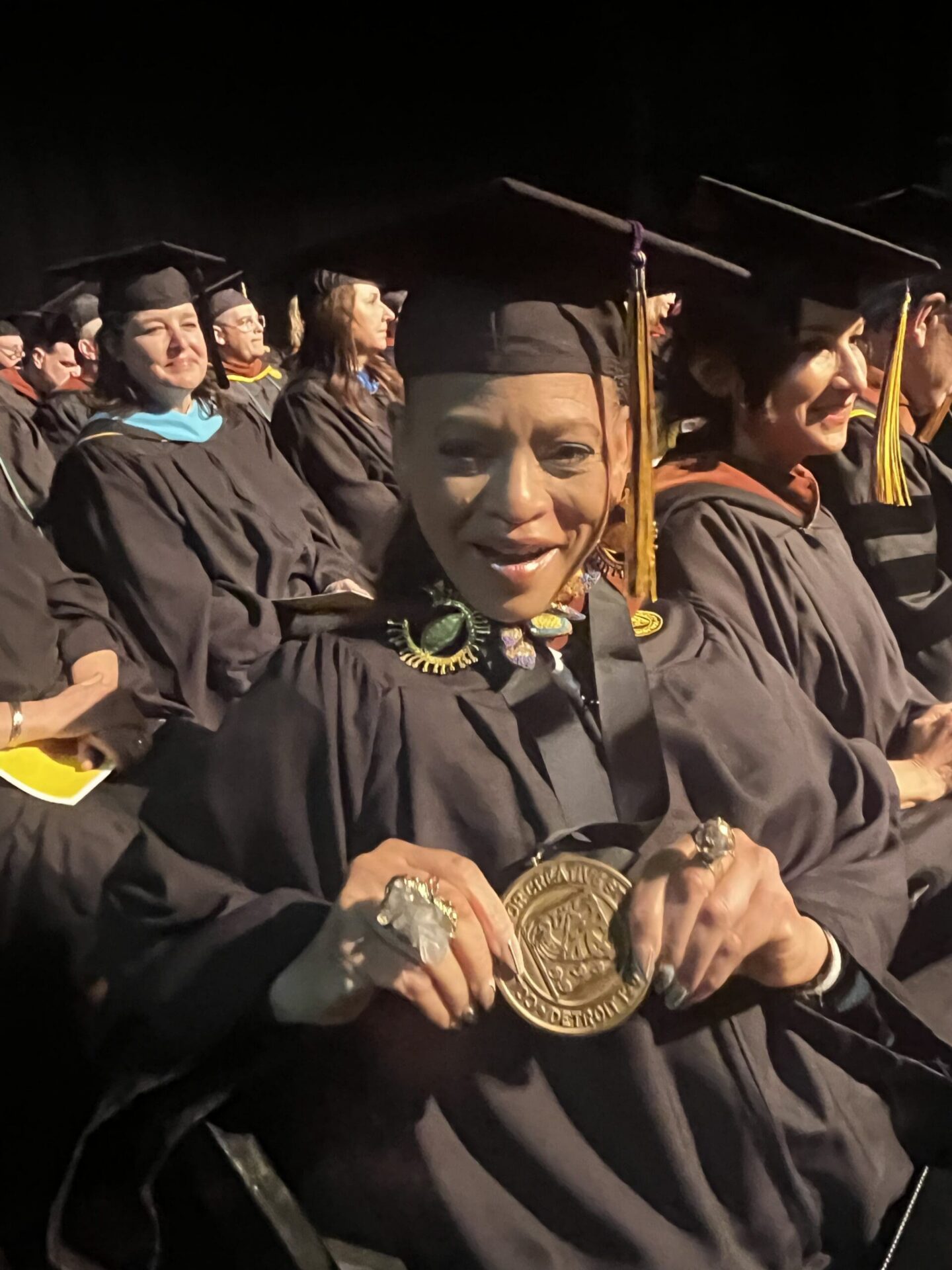 Sabrina Nelson holds her award while seated in commencement regalia.