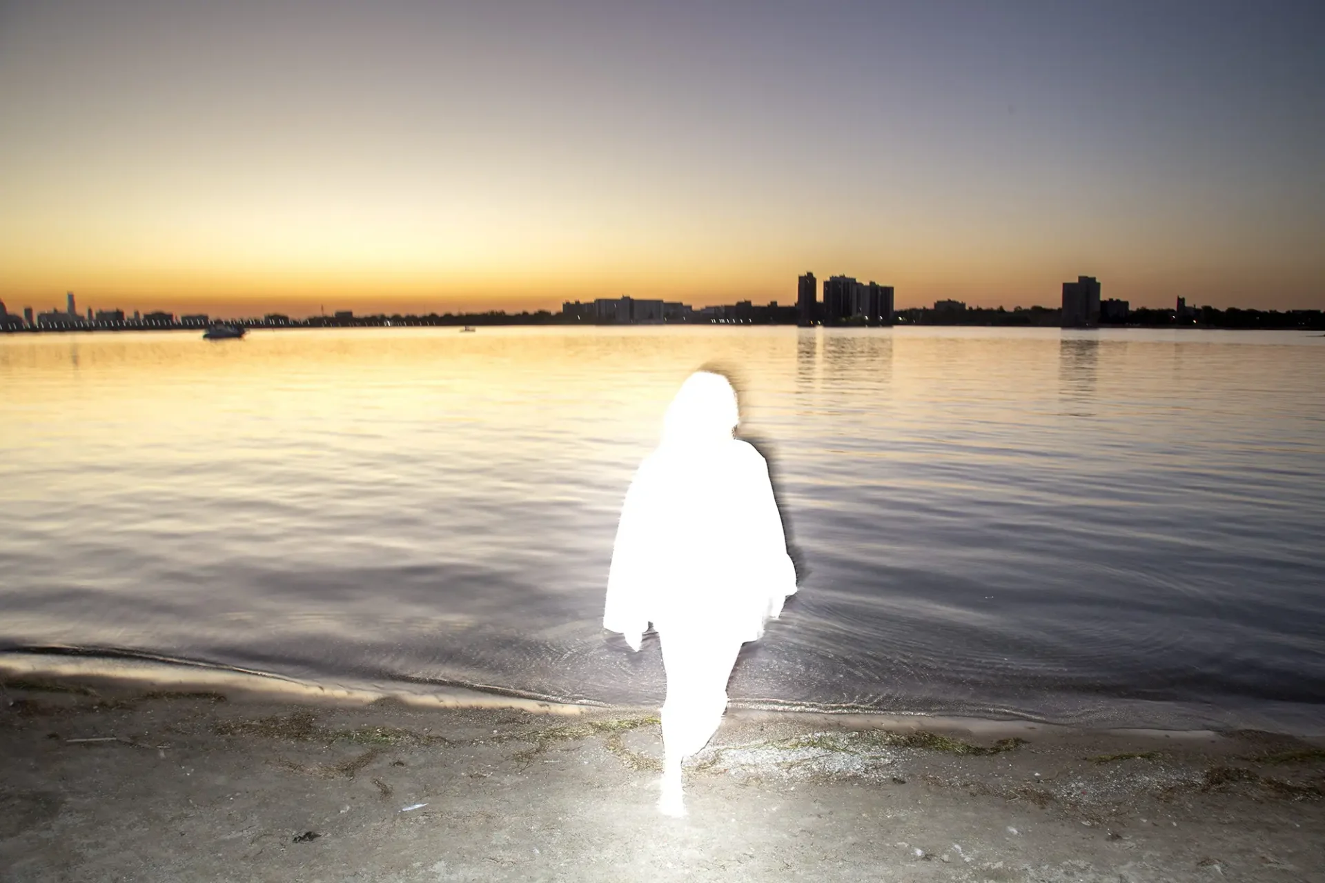 Solid white figure coming out of the water with a skyline in the distance.