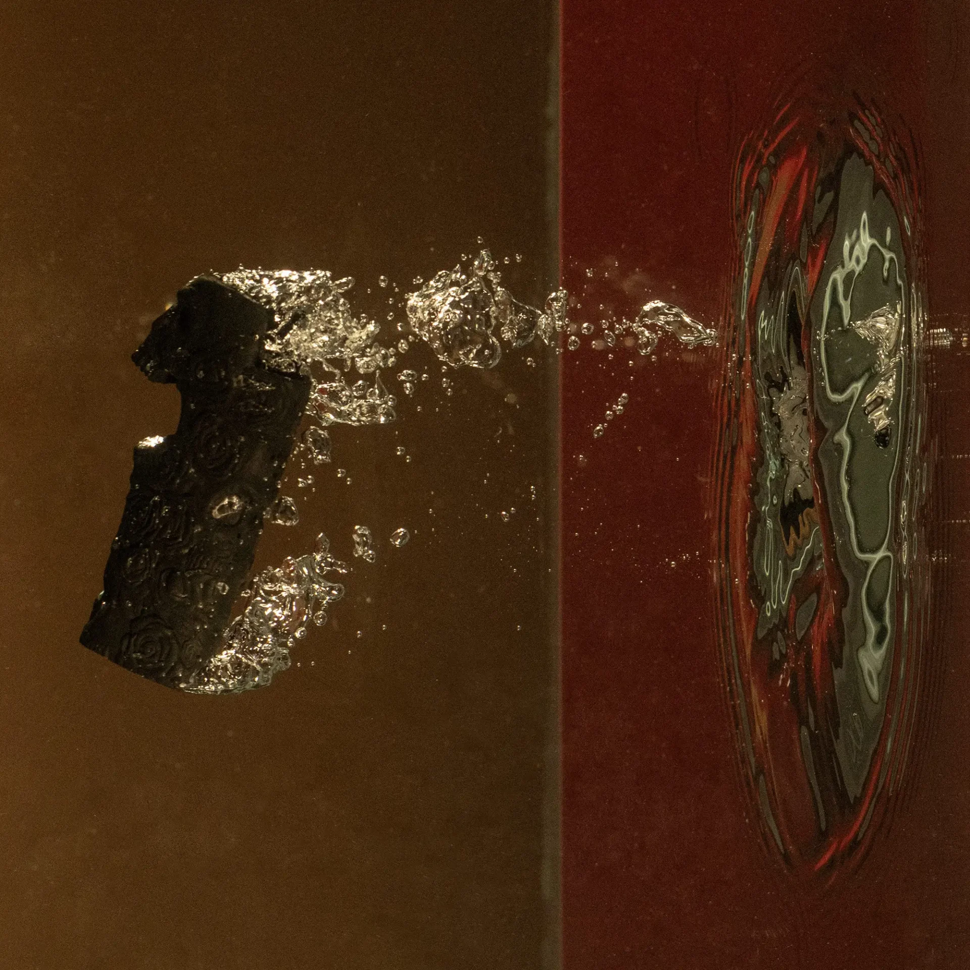 Photo of a black object splashing into water with a split green/red background.