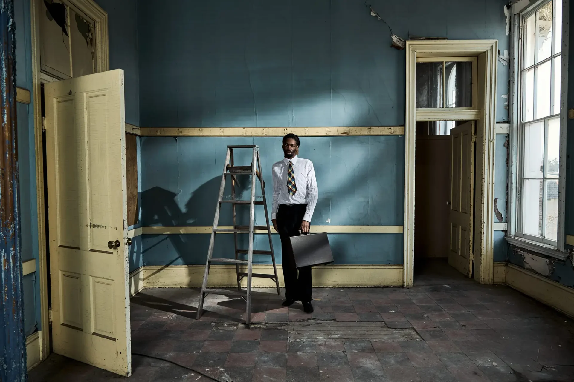 Environmental portrait of a young African-American man in business attire standing in a domestic interior under construction.