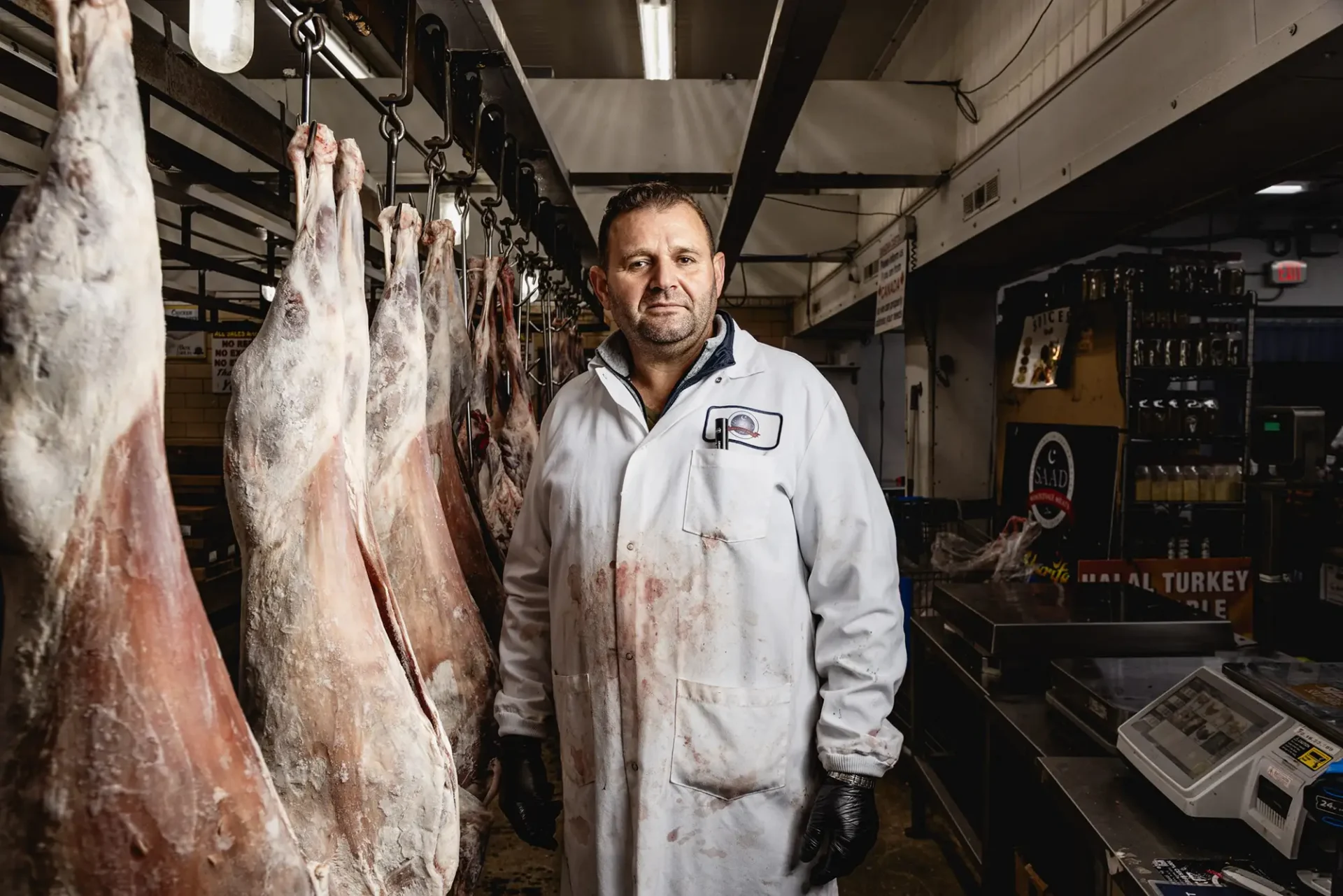 Environmental portrait of a butcher standing in front of "hanging weight" in his shop.