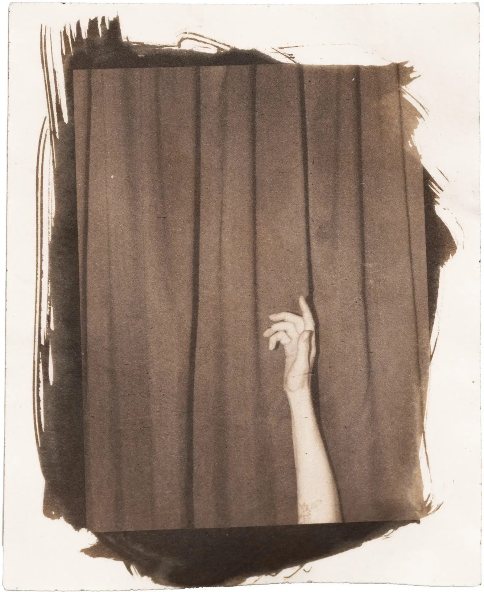 Van Dyke print of an arm in front of a curtain on cream drawing paper.